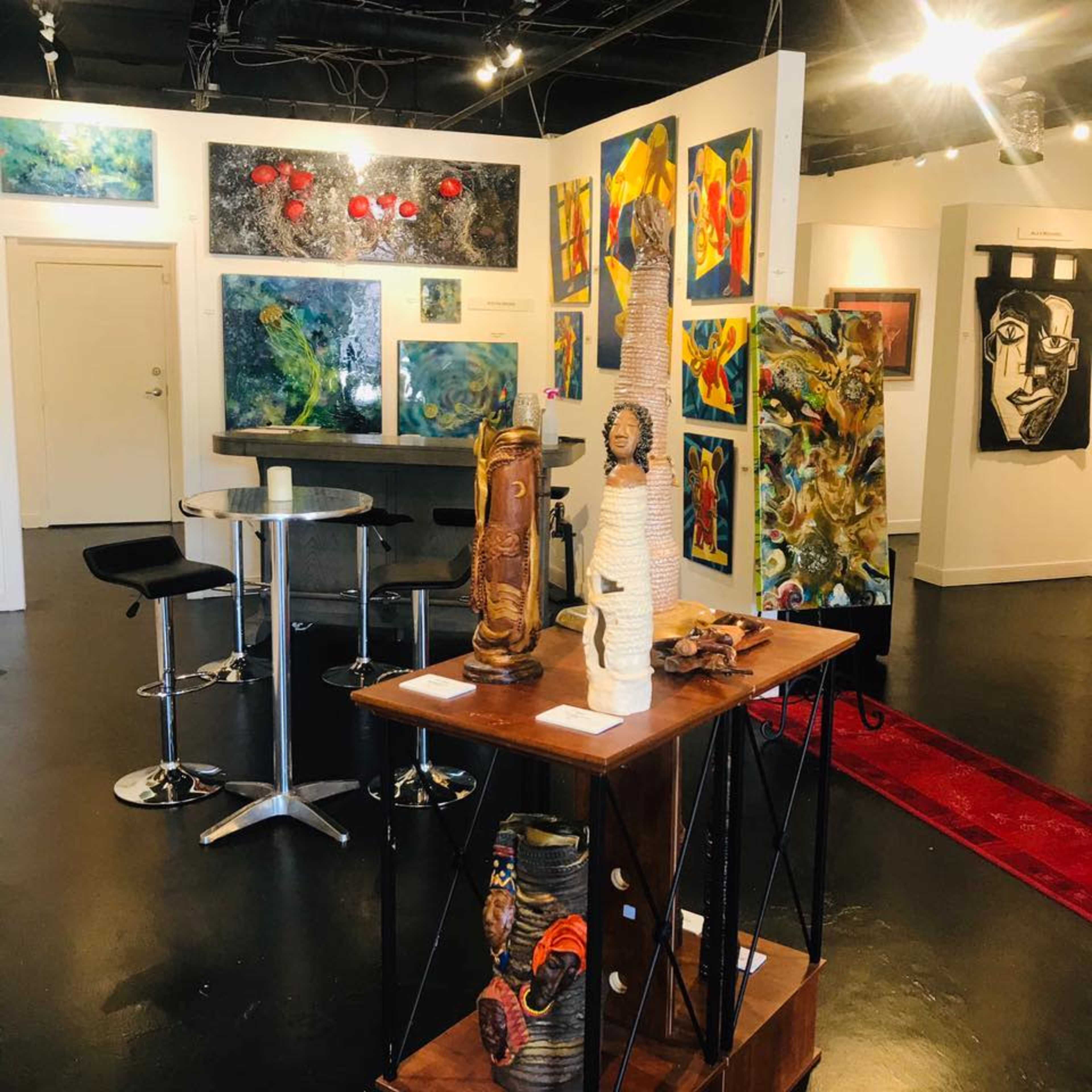 An art gallery with colorful paintings on the walls and various sculptures displayed on a central table.