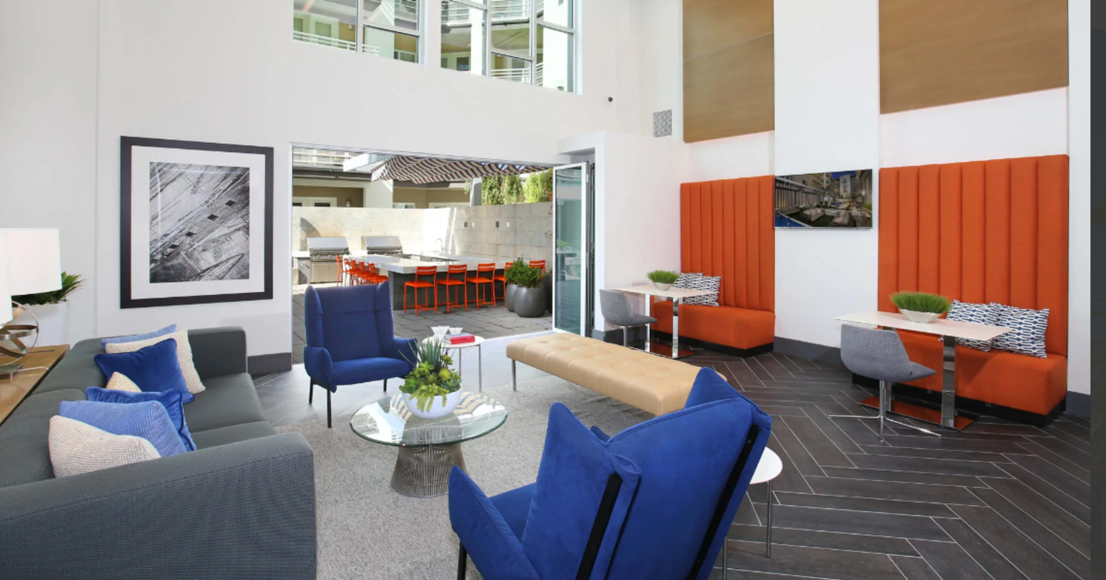 A modern lobby area with blue and orange seating, a coffee table, and large windows allowing natural light.