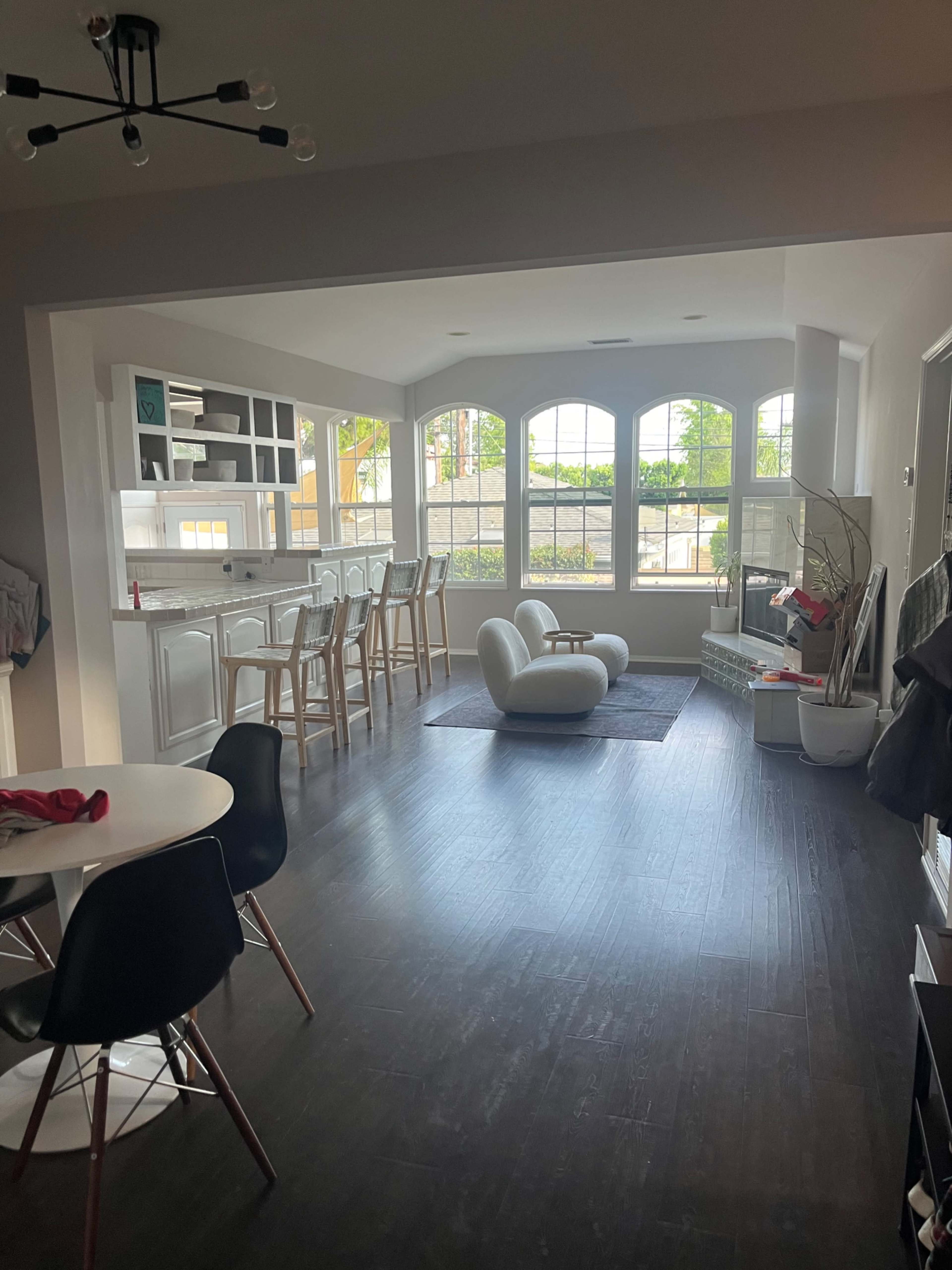 The image shows a spacious, modern living area with large windows, a dining table, and a white lounge chair.