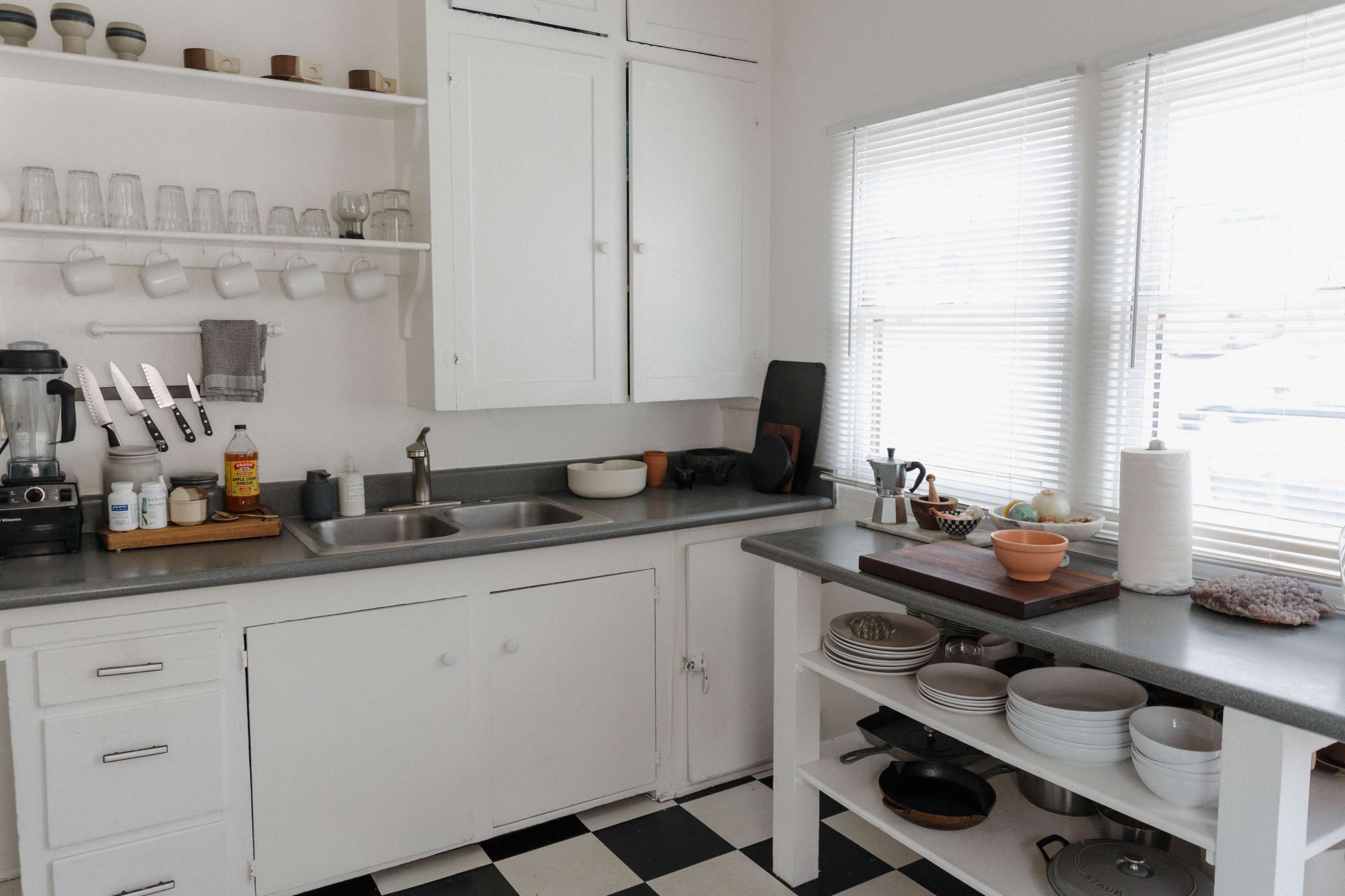 A modern kitchen features a gray countertop, white cabinets, and well-organized shelves with glassware and kitchen appliances.