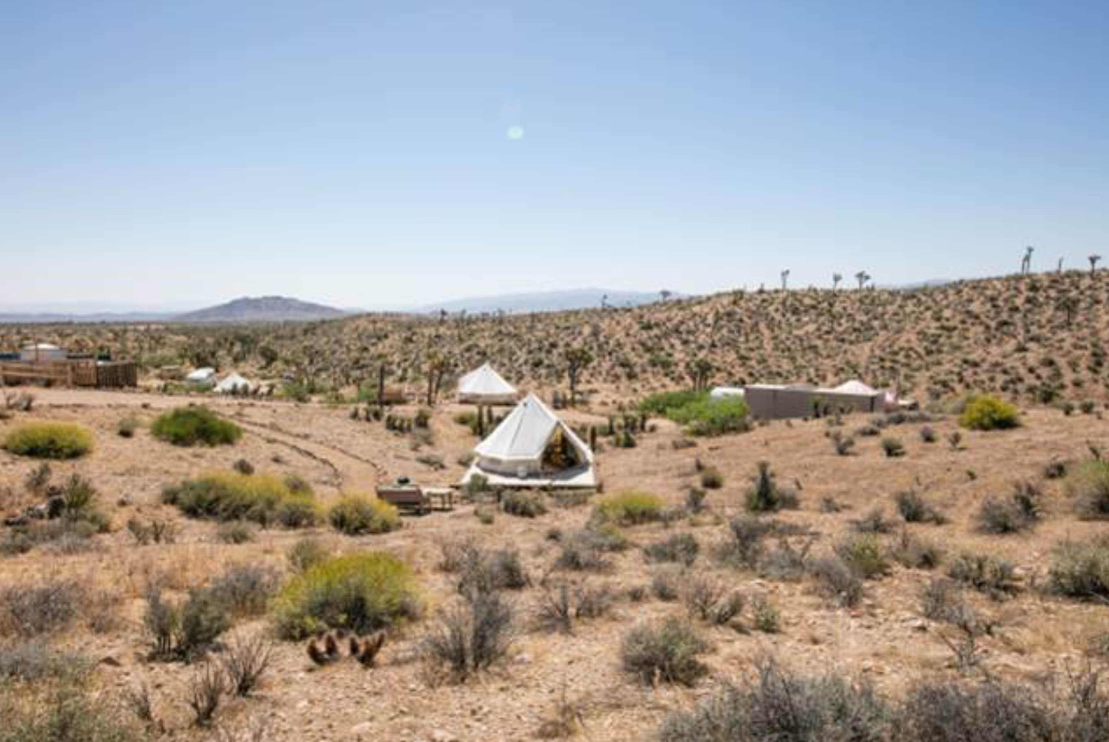 A series of tents are set up among sparse shrubs and rocky terrain in a desert landscape.