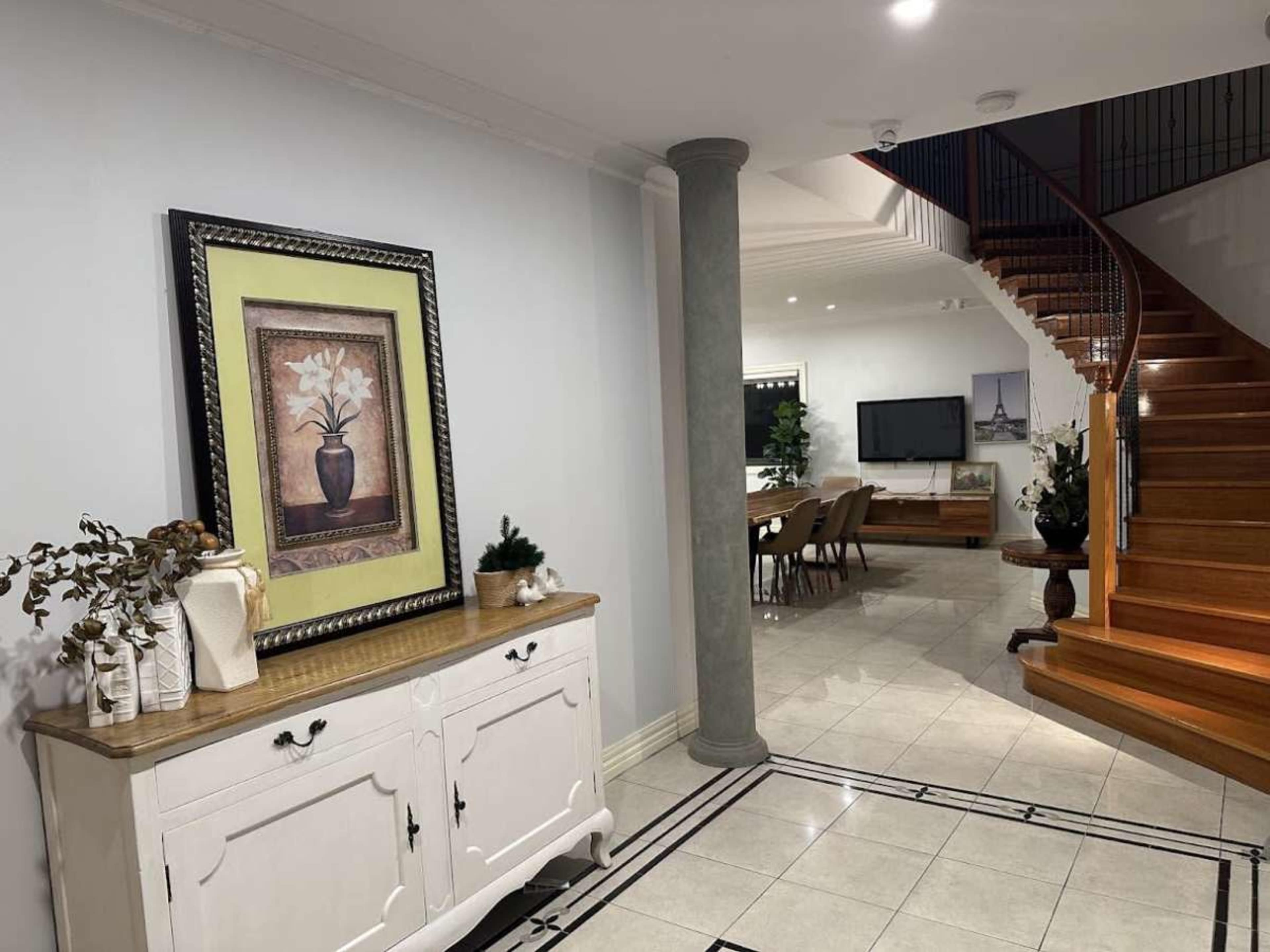 The image shows a modern home interior with a staircase leading to an upper floor, a framed artwork on the wall, and a decorative console table in the foreground.