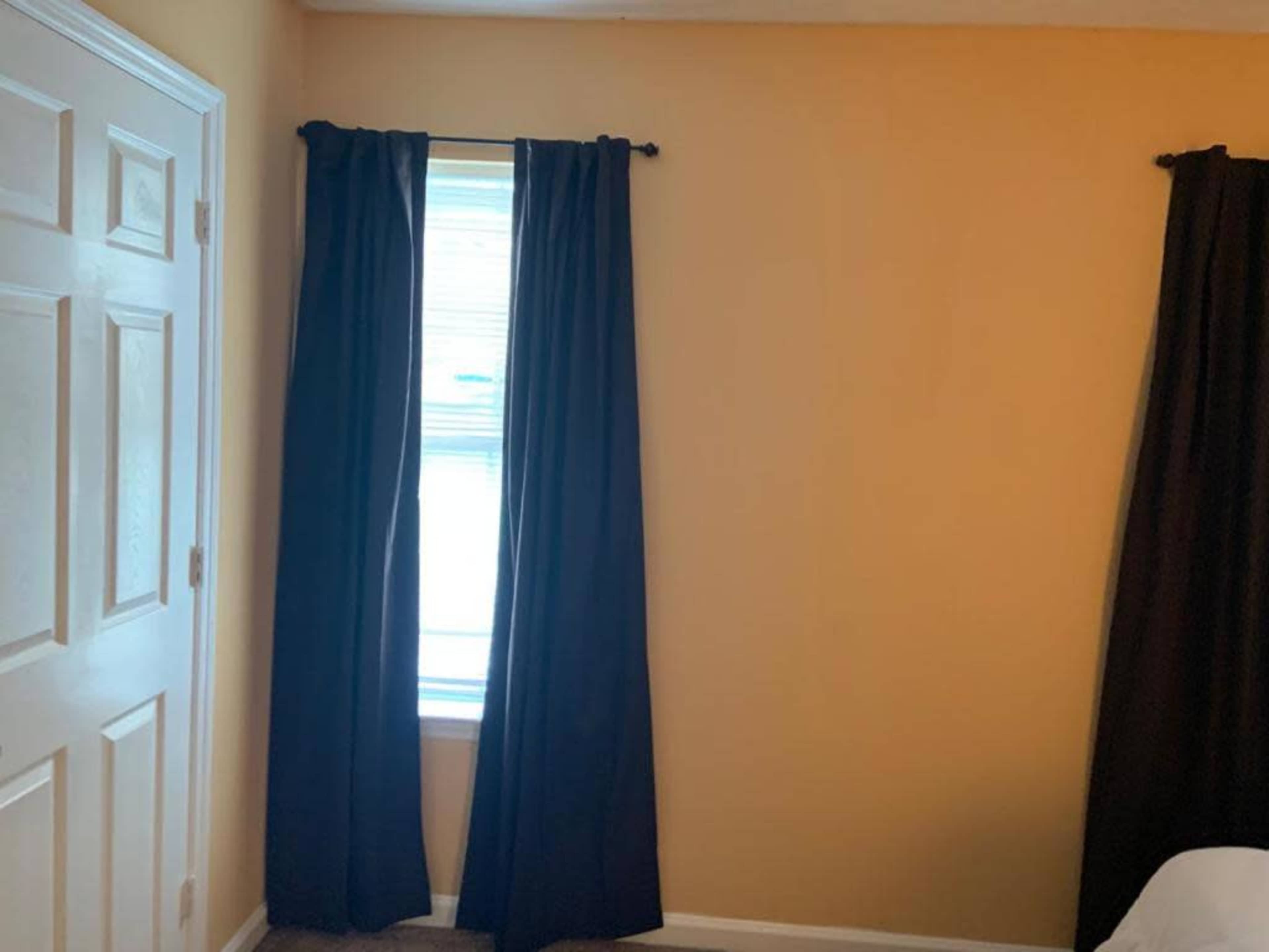 A room with yellow walls, a window dressed with black curtains, and a closed white door.