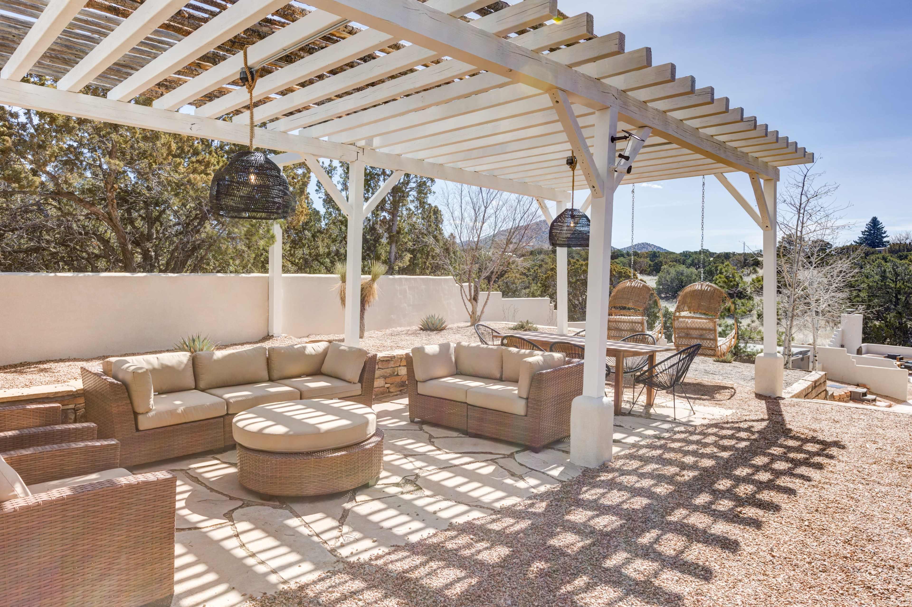 The image shows a spacious outdoor patio featuring a seating area with wicker furniture, a round coffee table, and a shaded pergola with hanging lights.