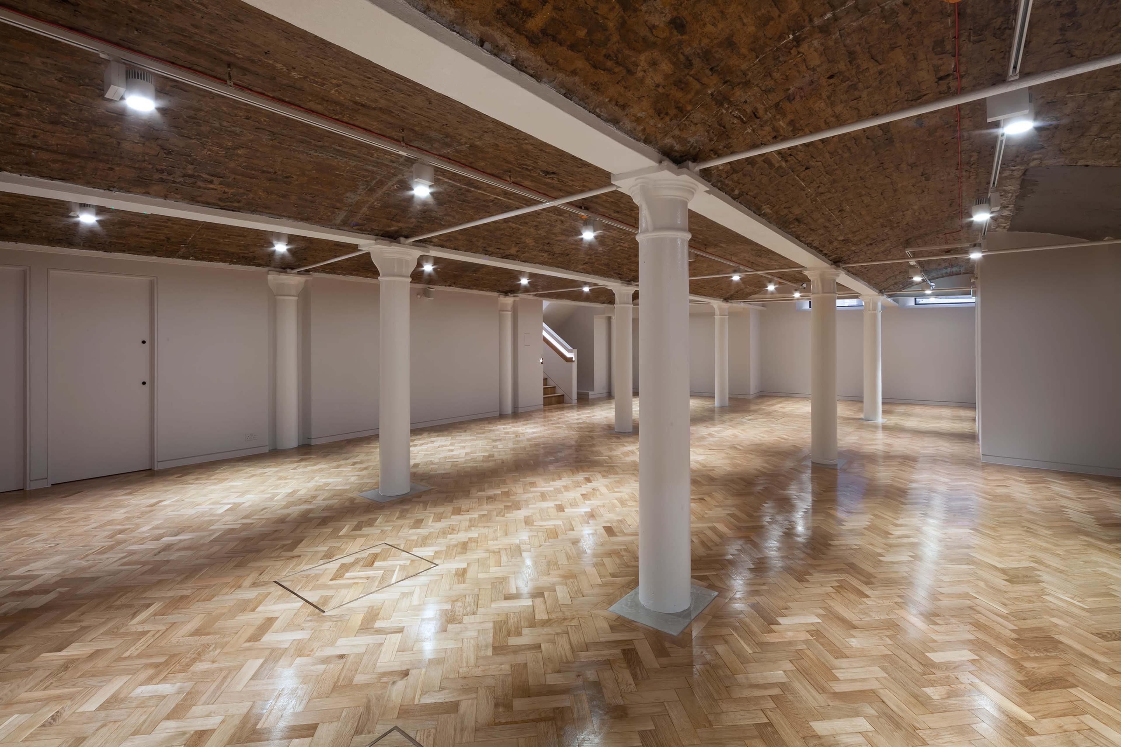 A spacious, empty room with wooden flooring and multiple white columns supporting a textured ceiling.
