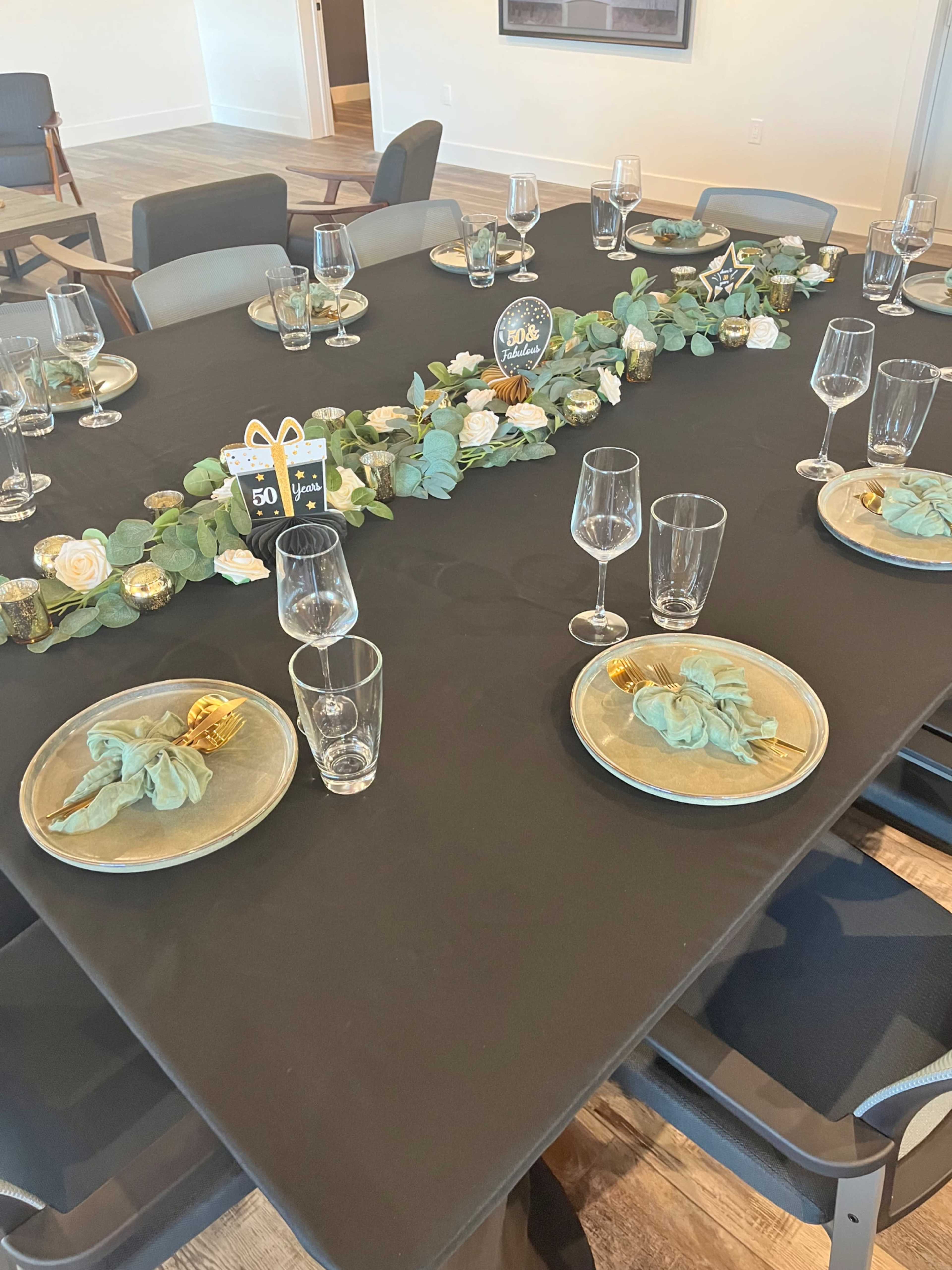 A dining table is set with plates, glasses, and a decorative floral centerpiece in a modern room.