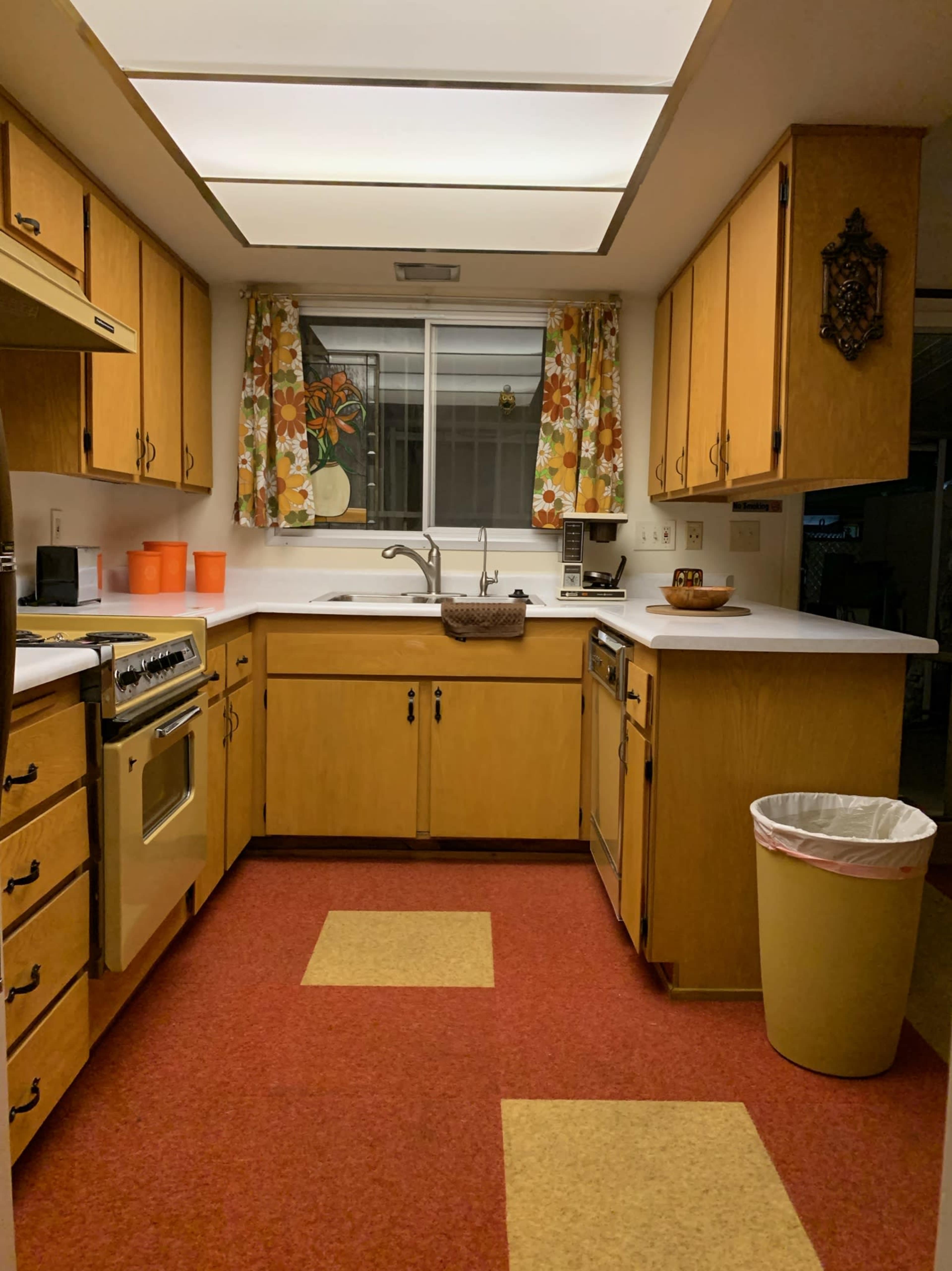 A kitchen with wooden cabinets, a white countertop, and a red and yellow patterned floor.