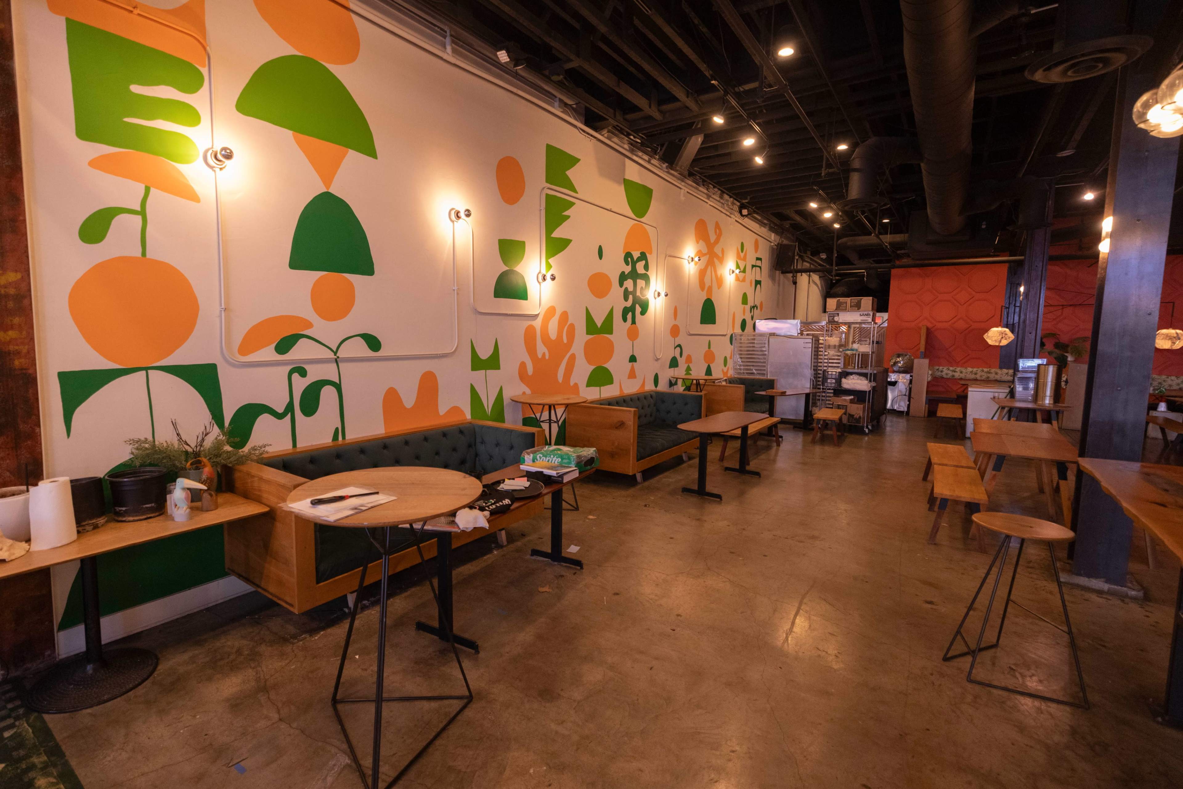 The image shows a brightly decorated café interior featuring a colorful mural on one wall, wooden tables, and seating arrangements.