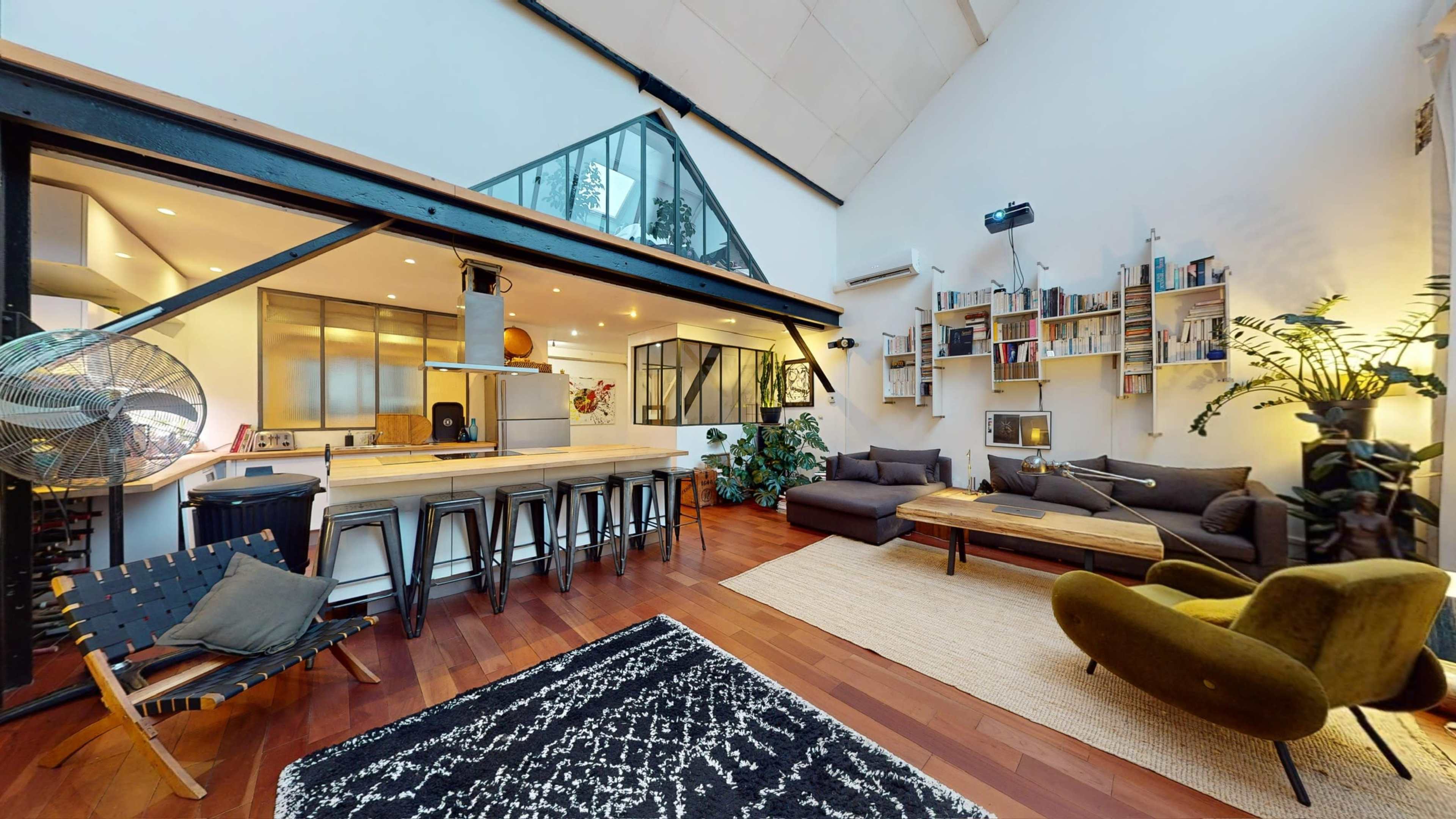 A spacious, modern living area with a kitchen, dining space, and a lounge featuring large windows and wooden flooring.