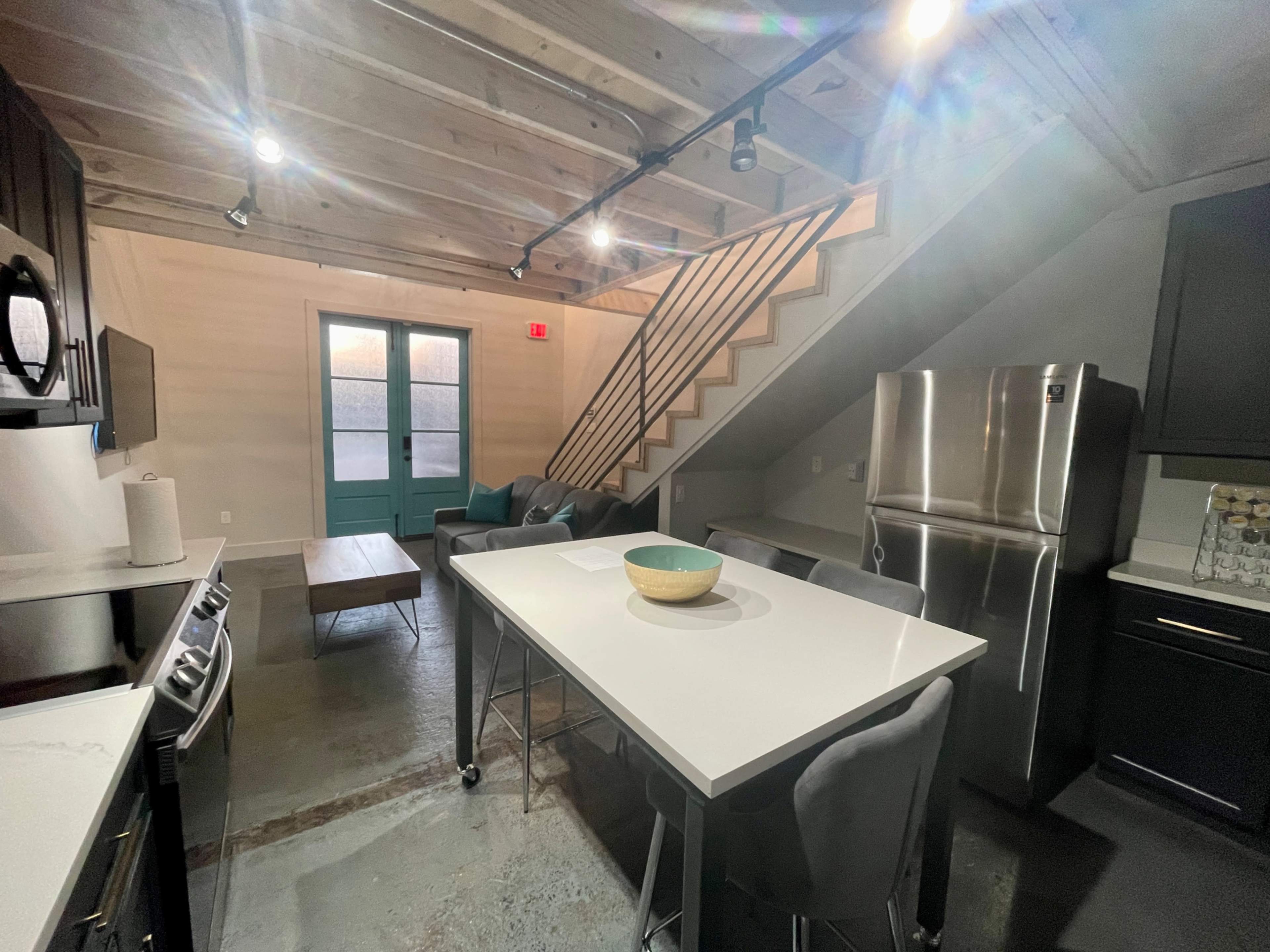 A modern kitchen with gray cabinetry, a large island with a bowl on it, and a staircase leading to an upper level.