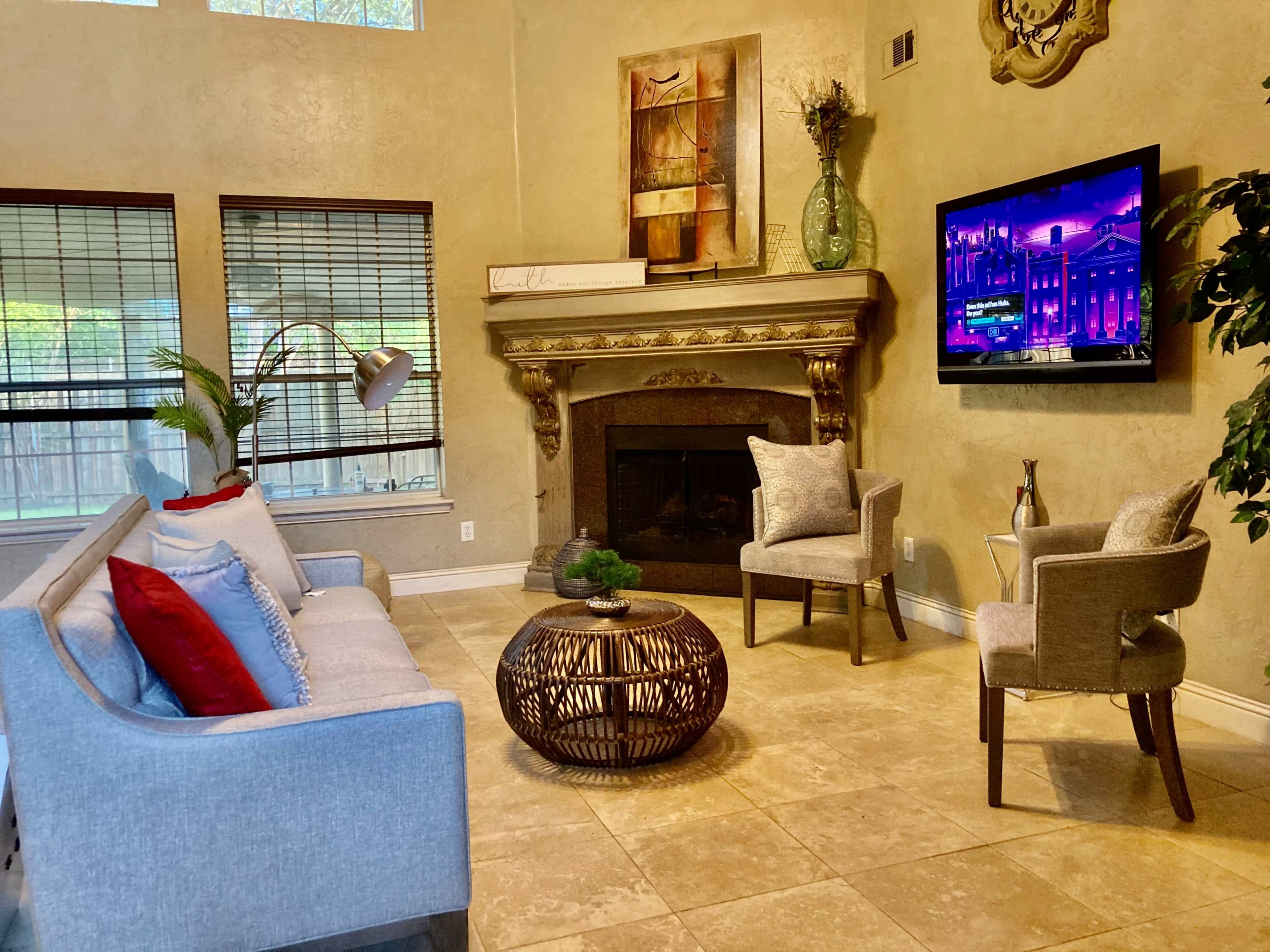 The living room features a gray sofa, two accent chairs, a round coffee table, a fireplace, and a television mounted on the wall.