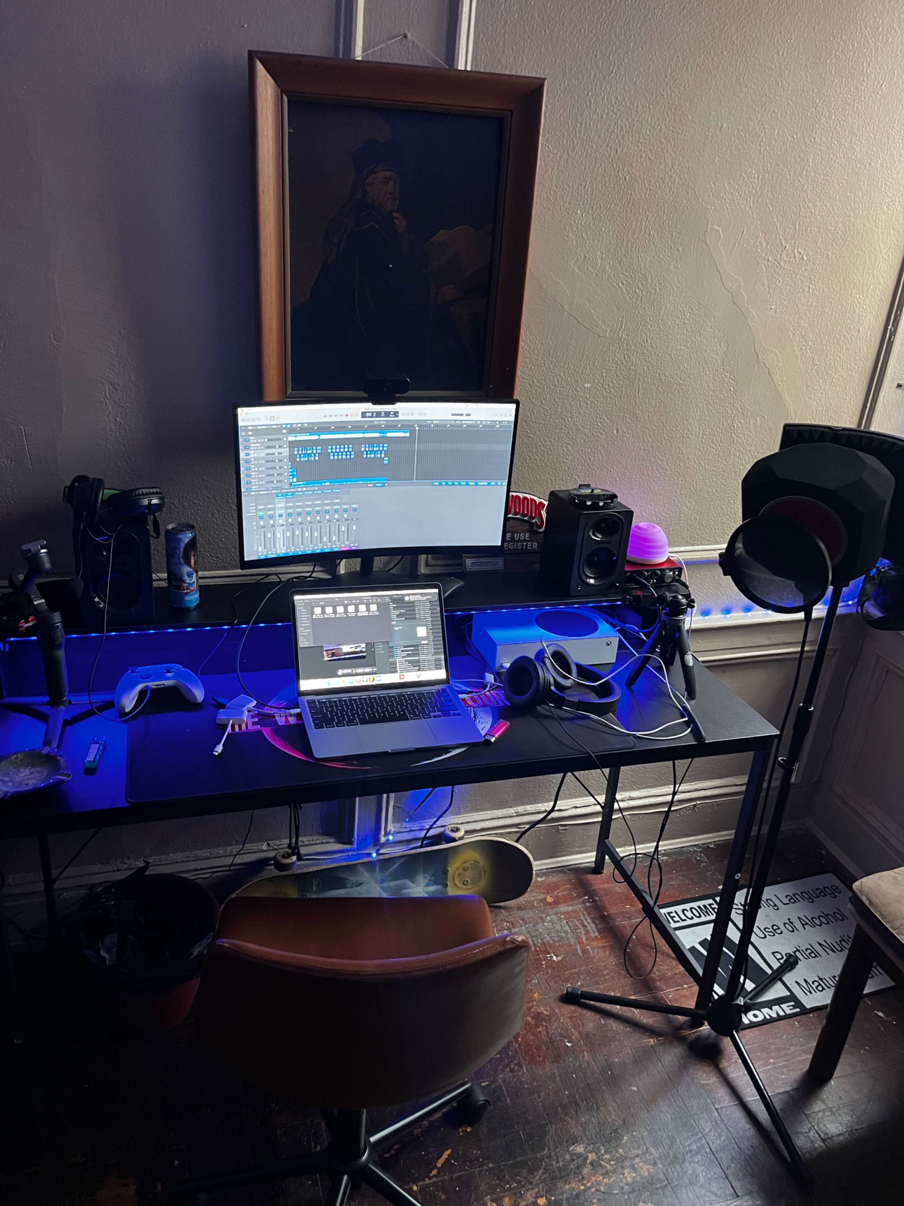 A home studio setup features a desk with a laptop, audio equipment, a monitor, and various accessories under soft lighting.