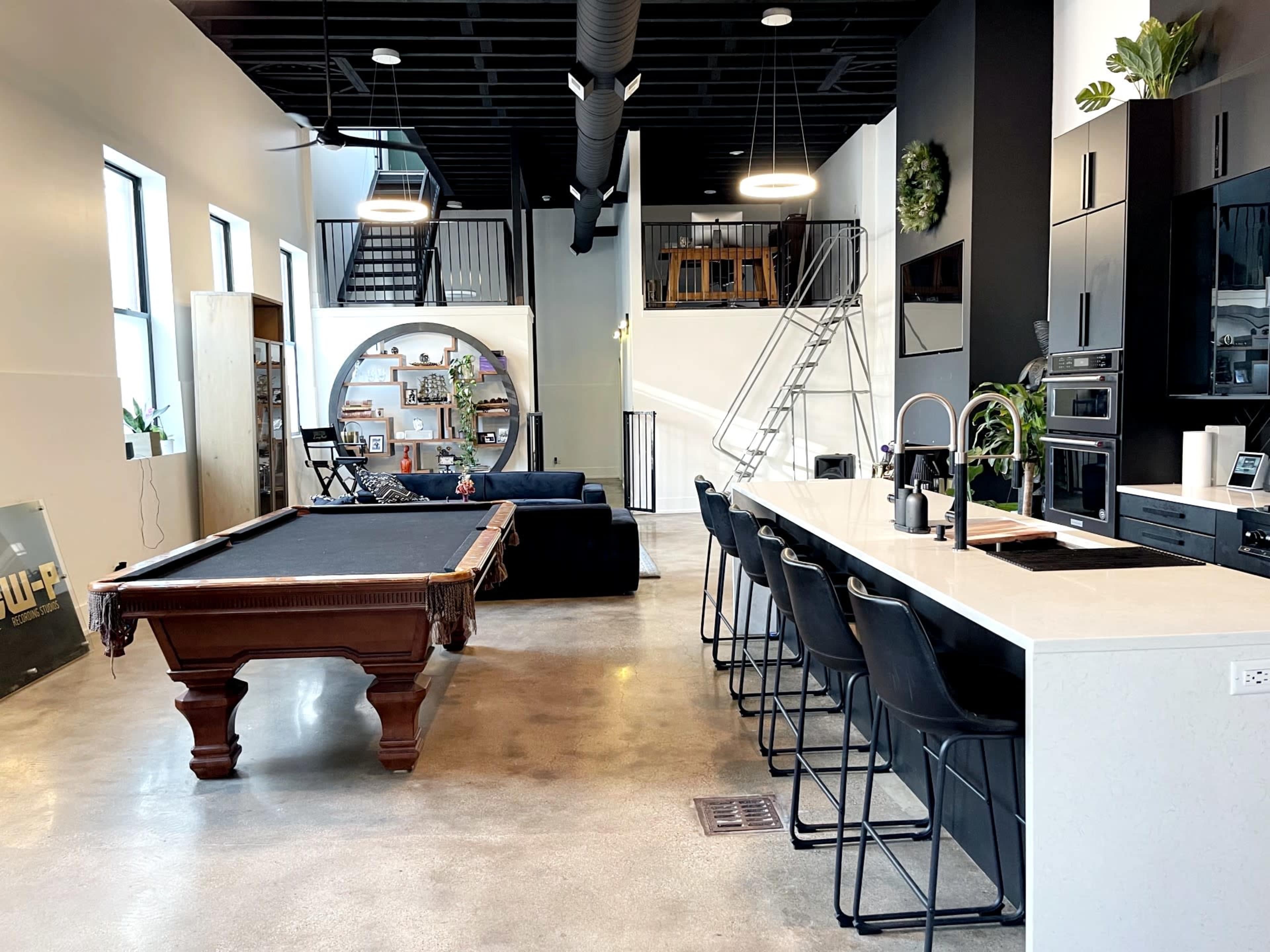 A modern open-concept living space featuring a pool table, a kitchen island with seating, and a staircase leading to an upper level.