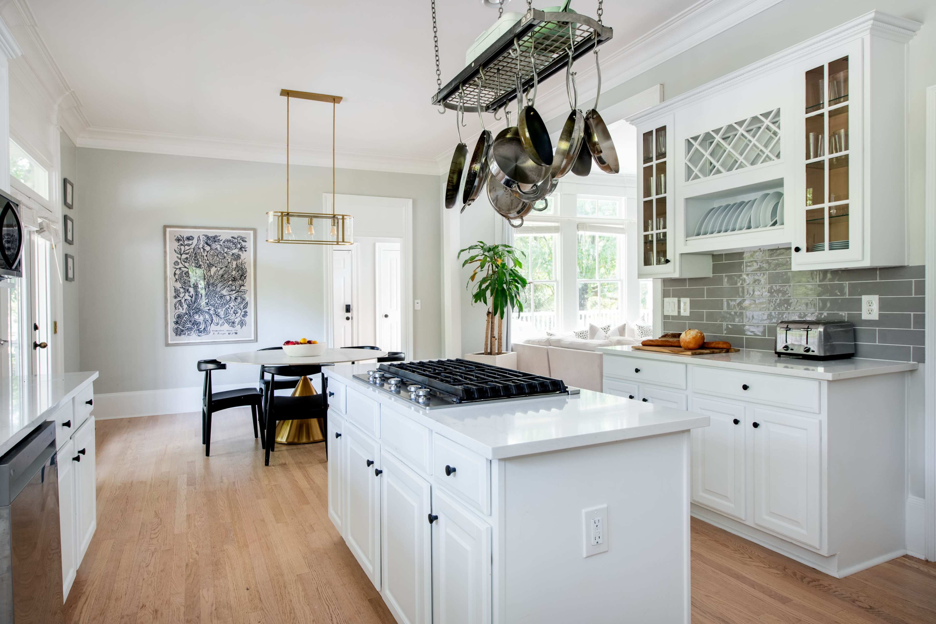 A bright kitchen features white cabinetry, a central island with a stovetop, and an overhead rack with hanging pots.