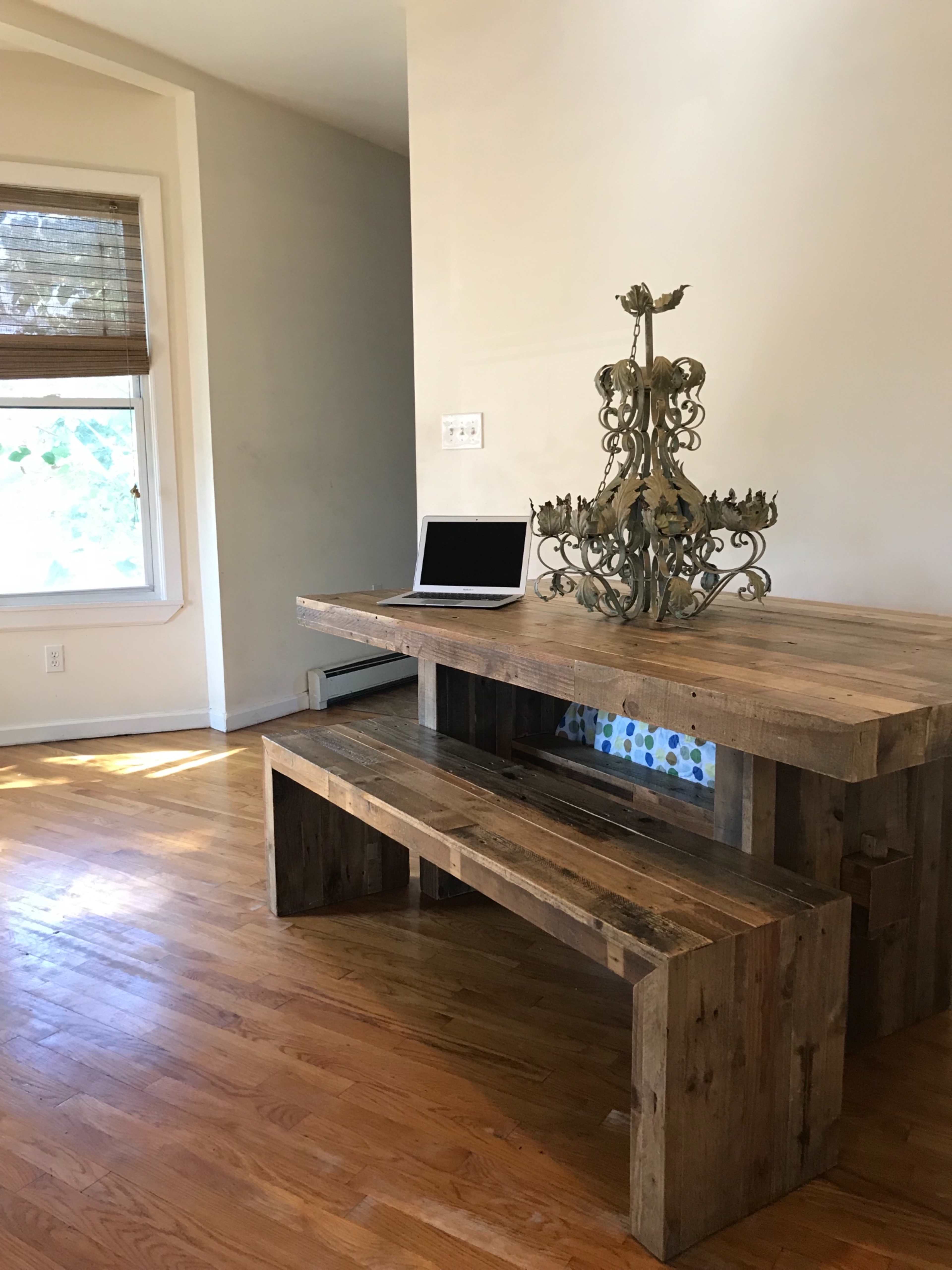 A wooden table with a decorative centerpiece and a laptop sits next to a window in a room with hardwood floors.