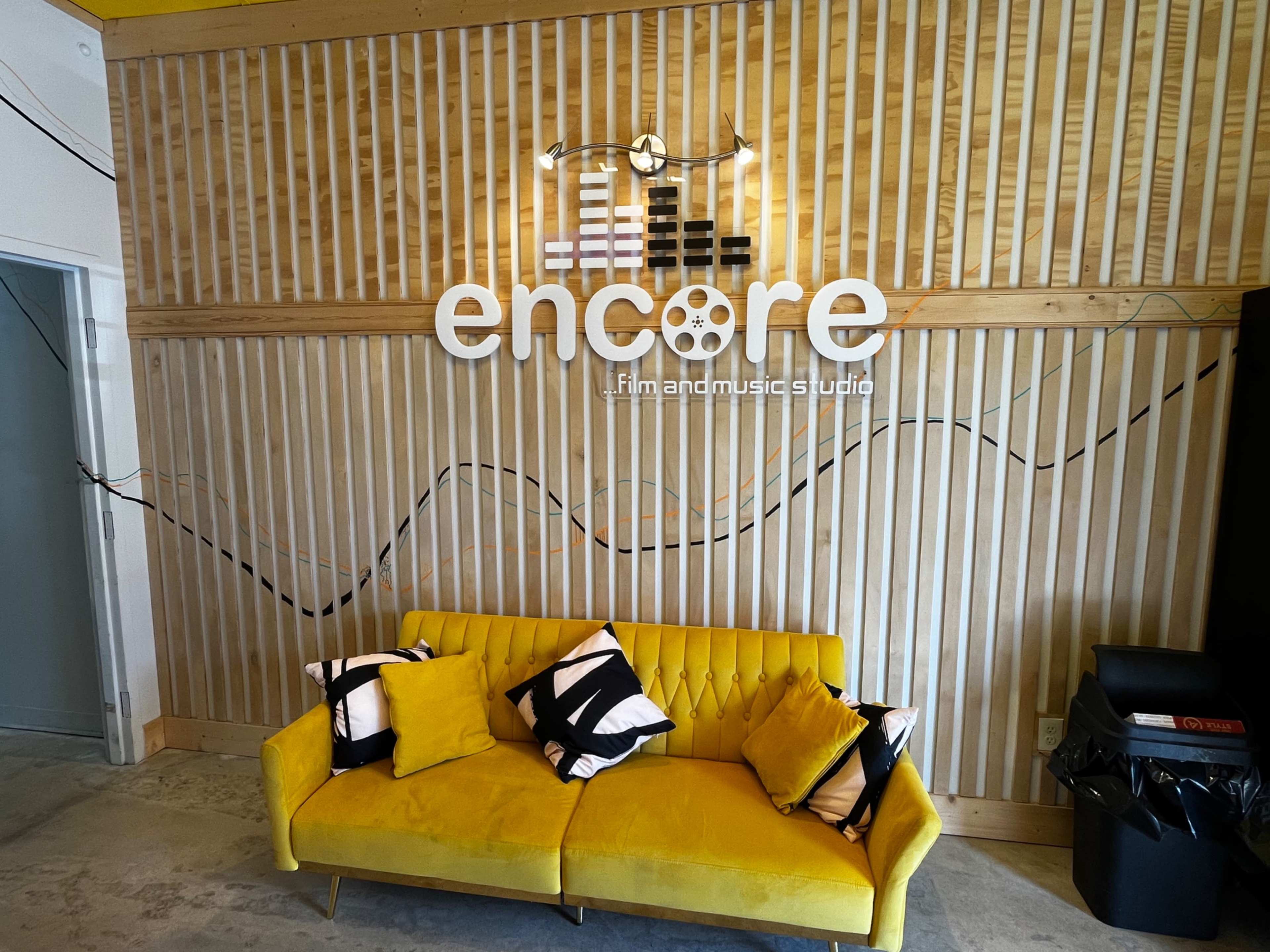 The image shows a bright yellow couch in front of a wooden wall with a sign that reads "encore fm and music studio."
