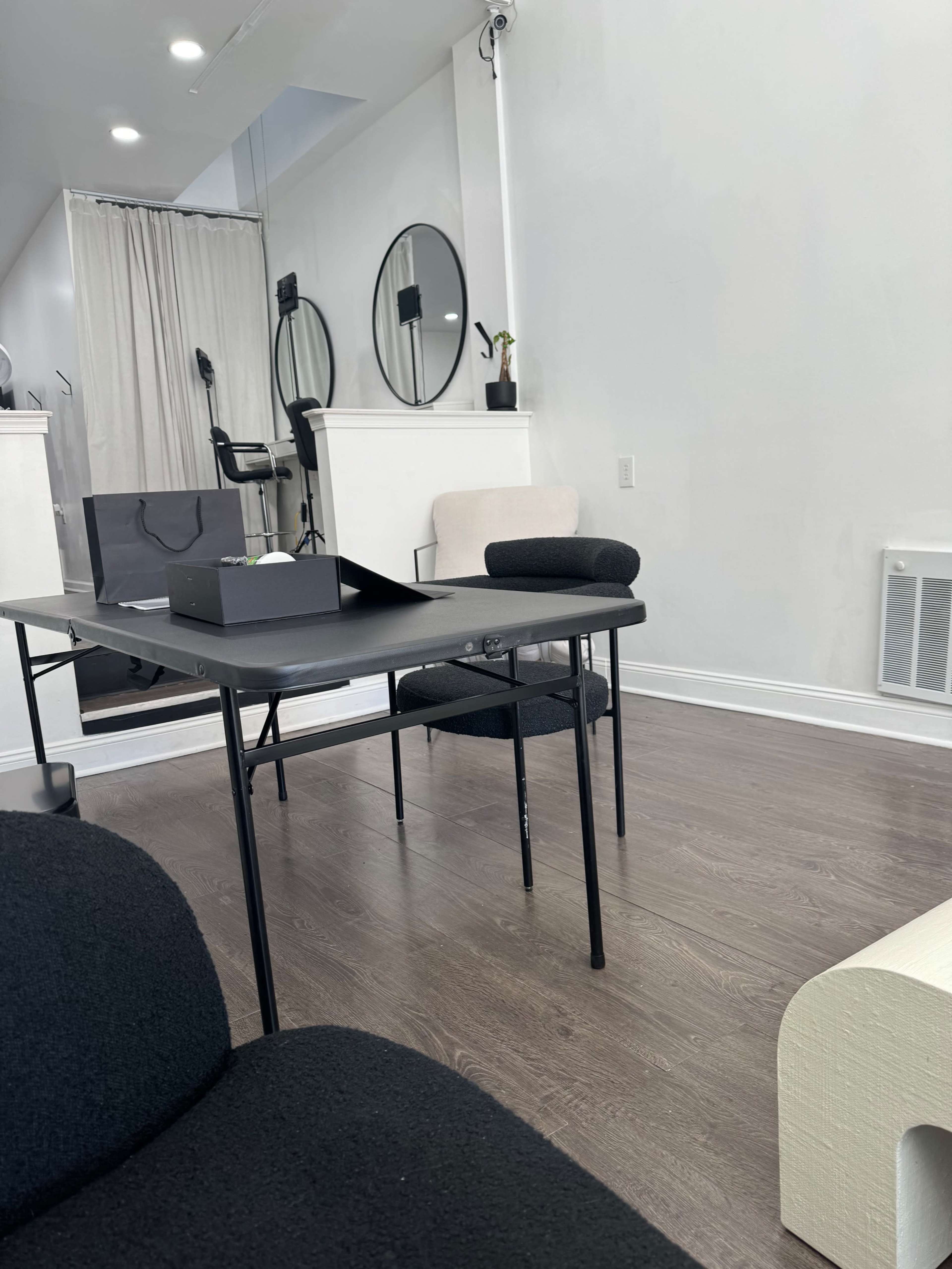 A minimalist indoor space featuring a black table and chairs, with mirrors on the walls and soft lighting.