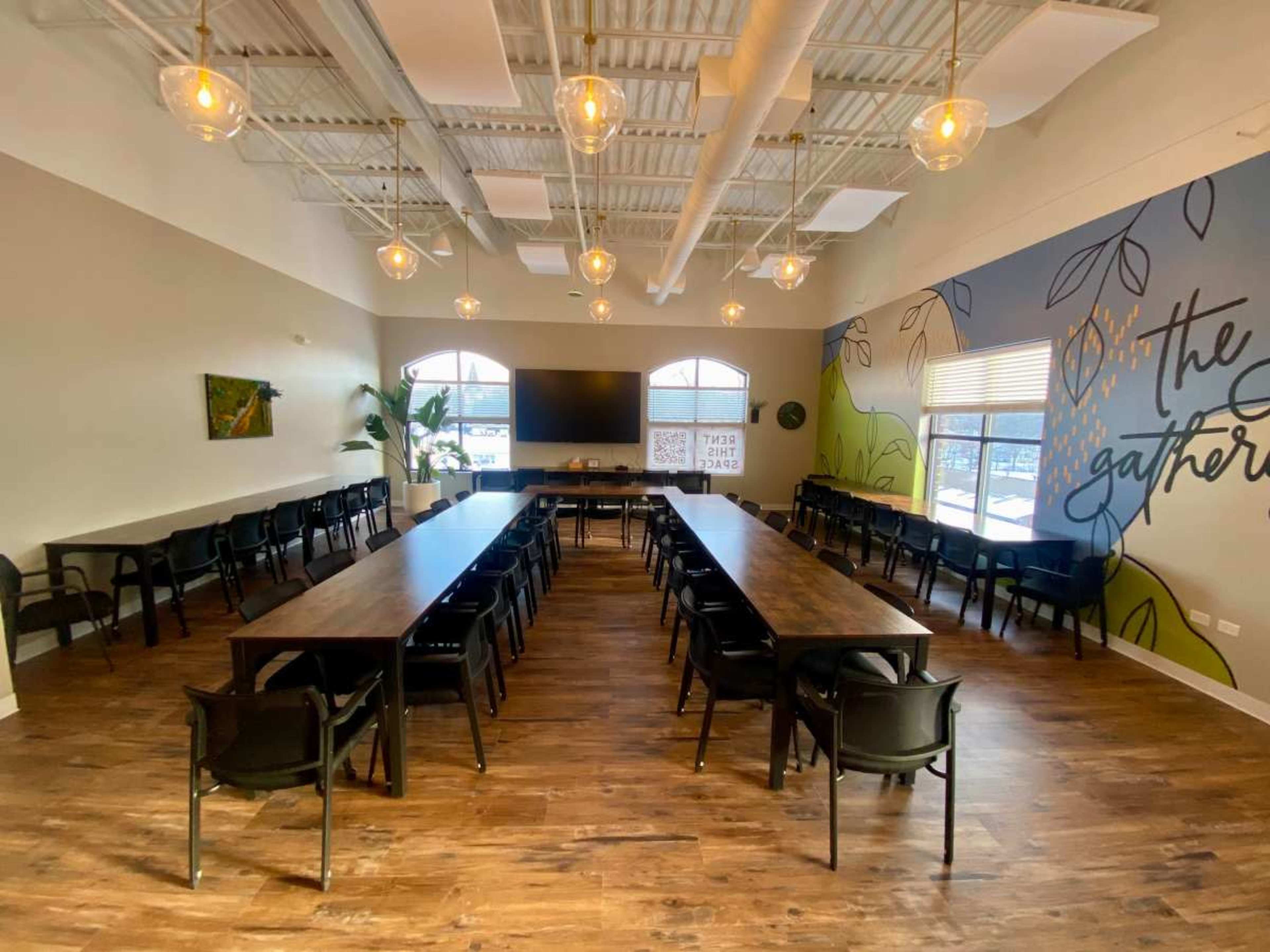 A meeting room features a long table surrounded by chairs, with large windows and decorative wall art.