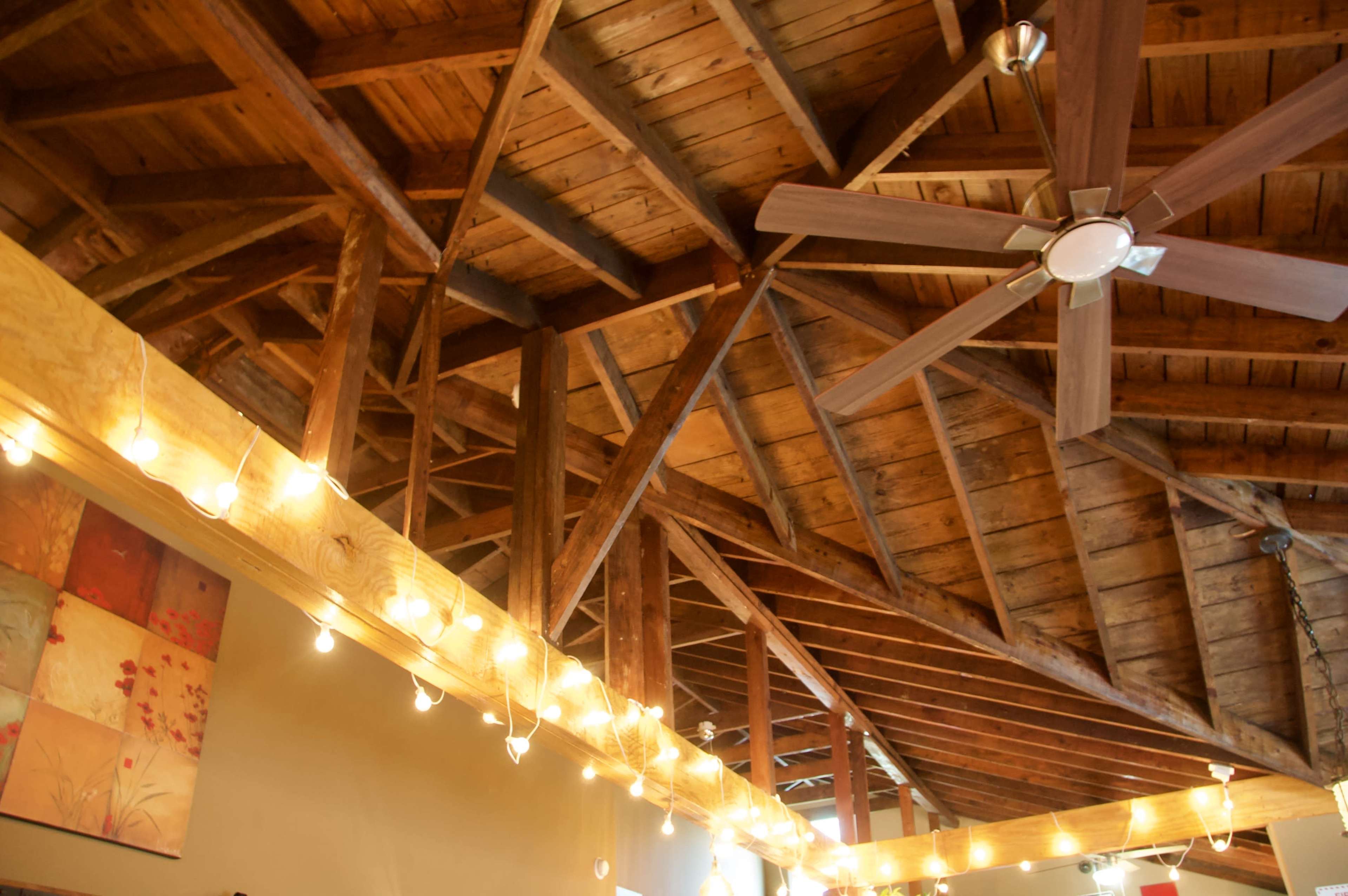 The image shows a wooden ceiling with exposed beams and a ceiling fan, illuminated by string lights.