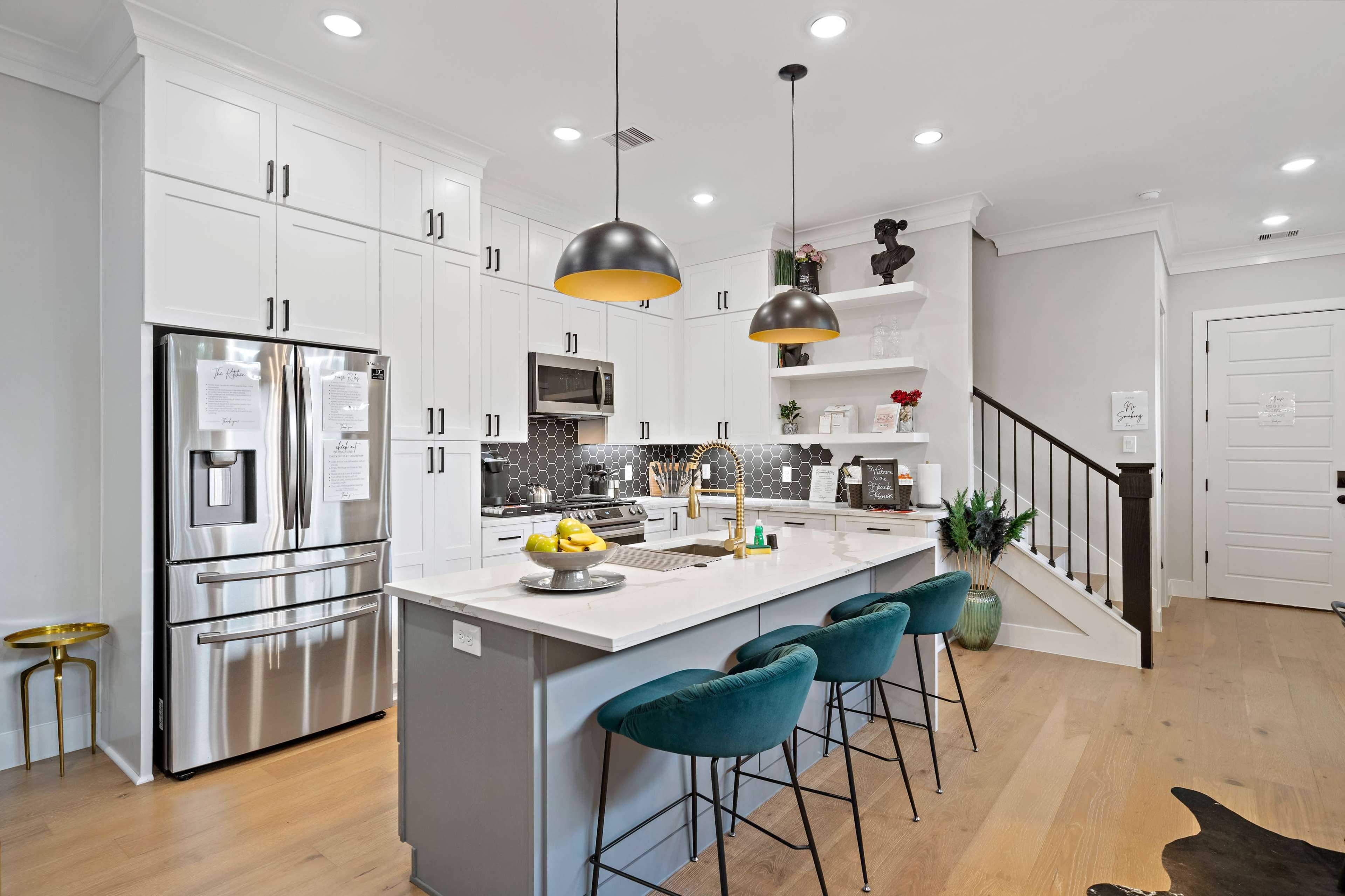 A modern kitchen features white cabinetry, stainless steel appliances, a large island with seating, and decorative pendant lighting.