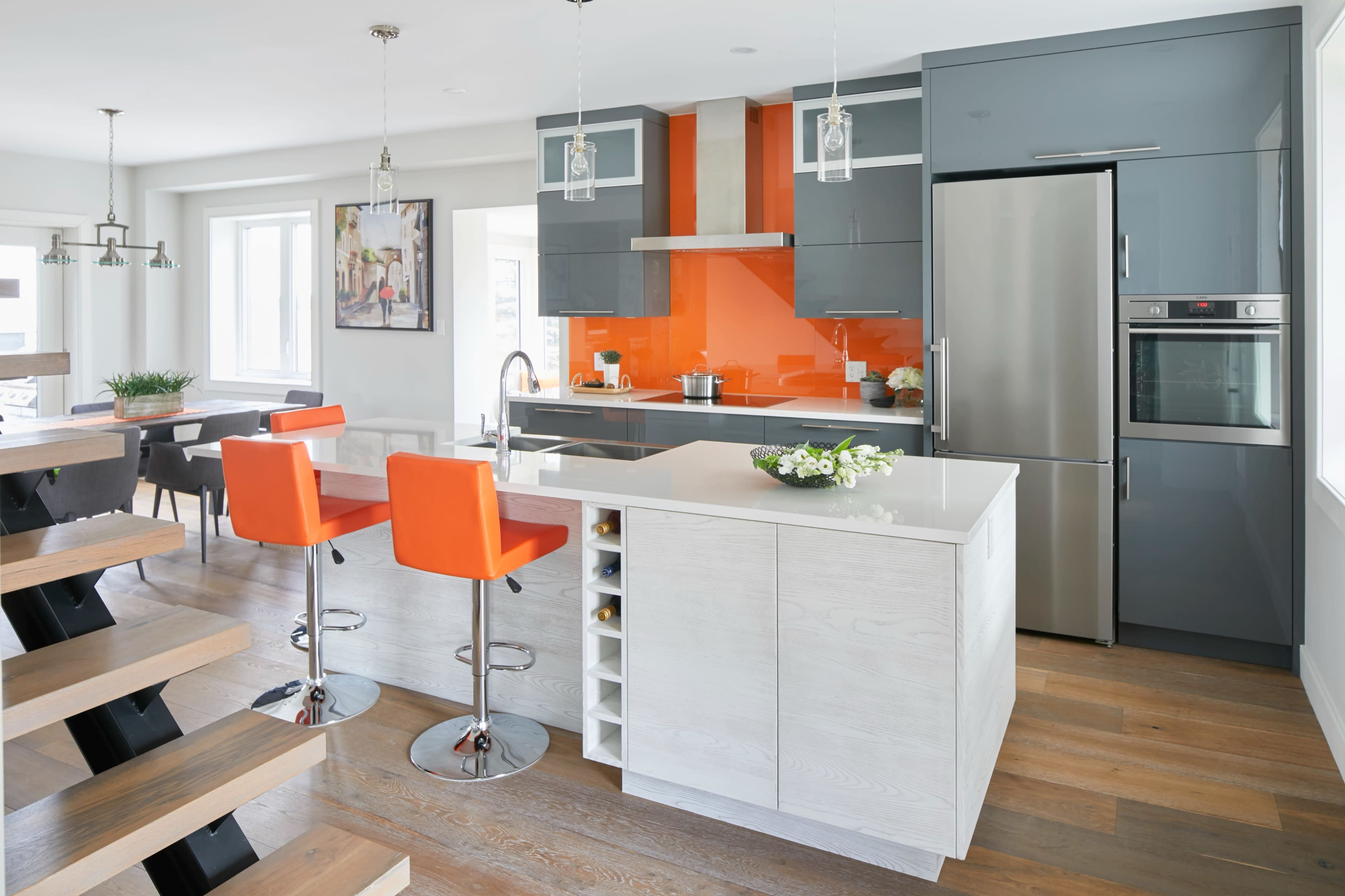 The kitchen features modern cabinetry in gray and light wood, an orange backsplash, and a central island with seating for two.