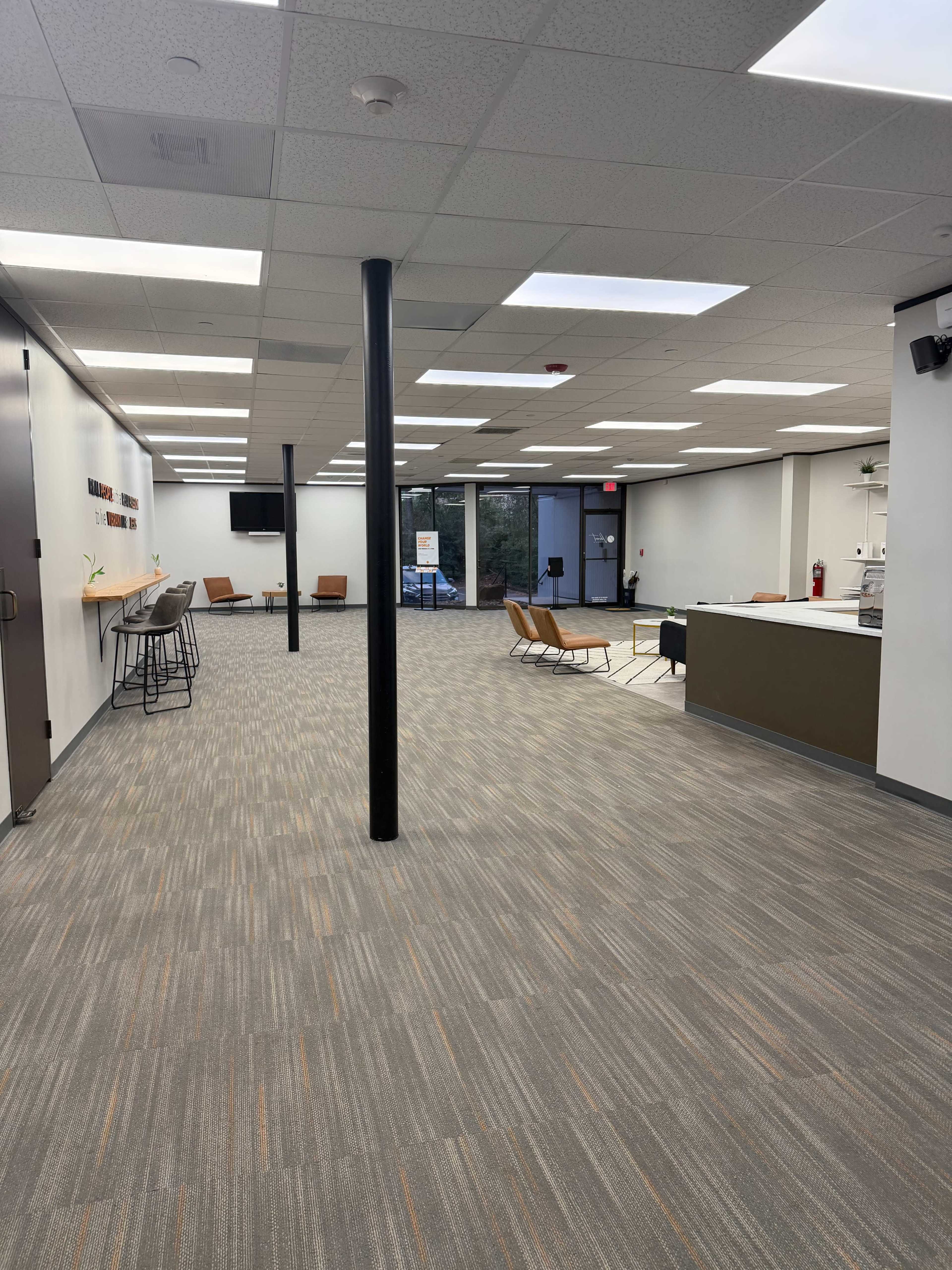 The image shows a spacious, modern office interior with a carpeted floor, several seating areas, and a reception desk.
