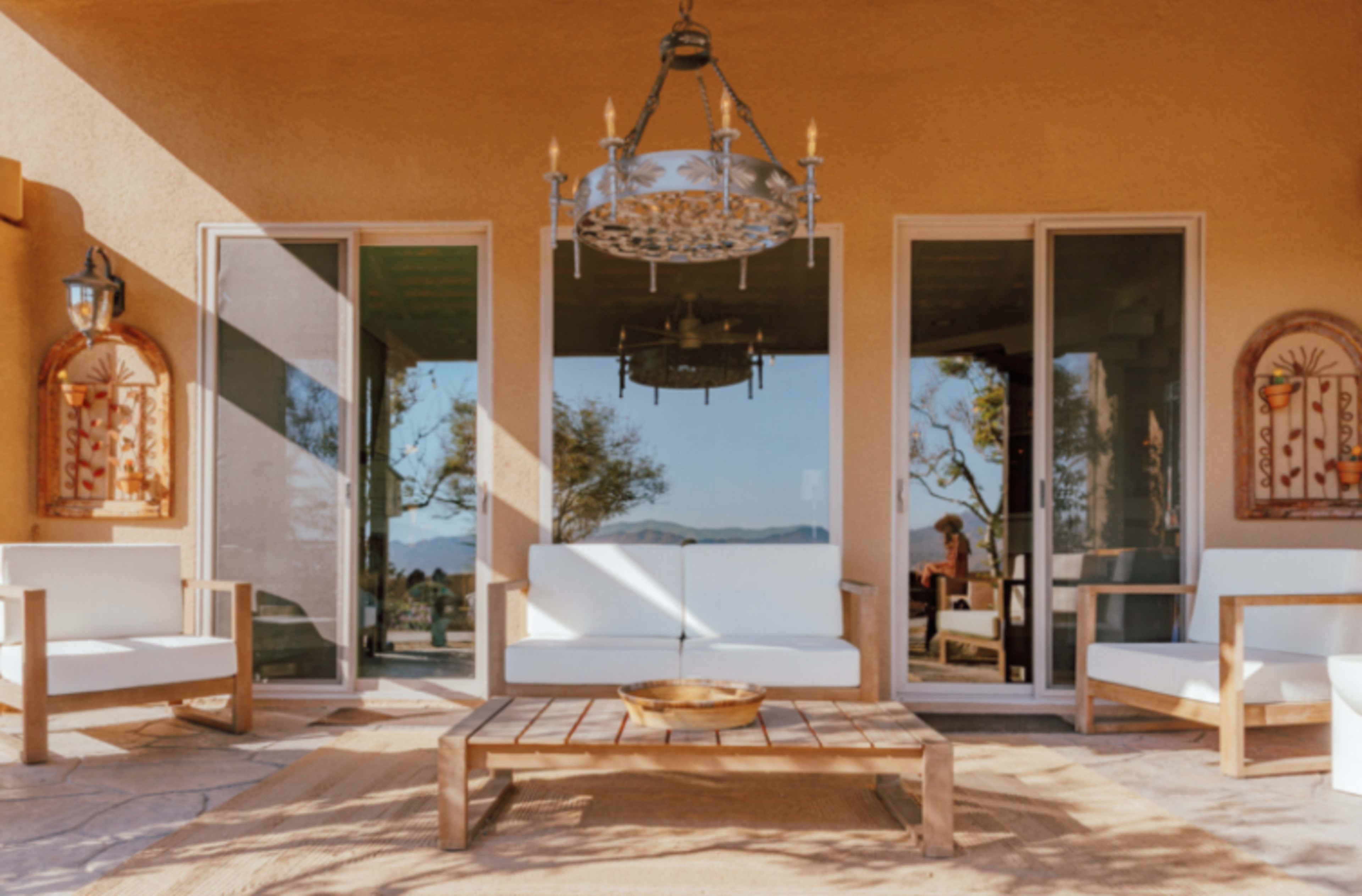 The image shows a cozy outdoor patio with white sofas and a wooden coffee table, illuminated by afternoon sunlight.