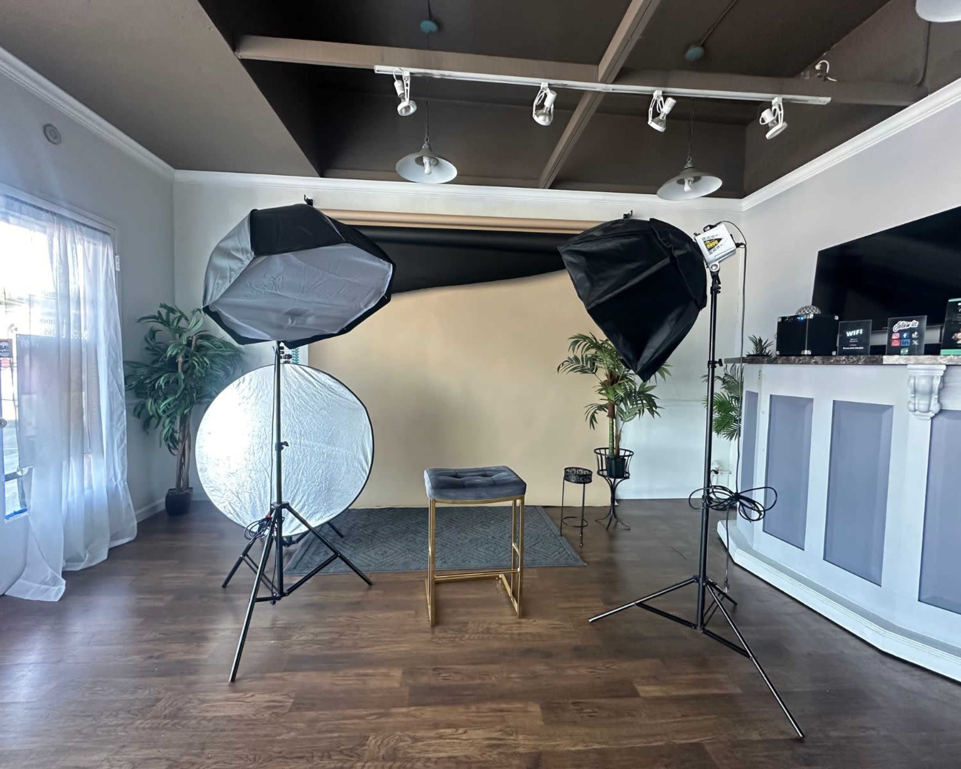A photography studio setup with two softboxes, a reflective umbrella, a stool, and a backdrop on a wooden floor.