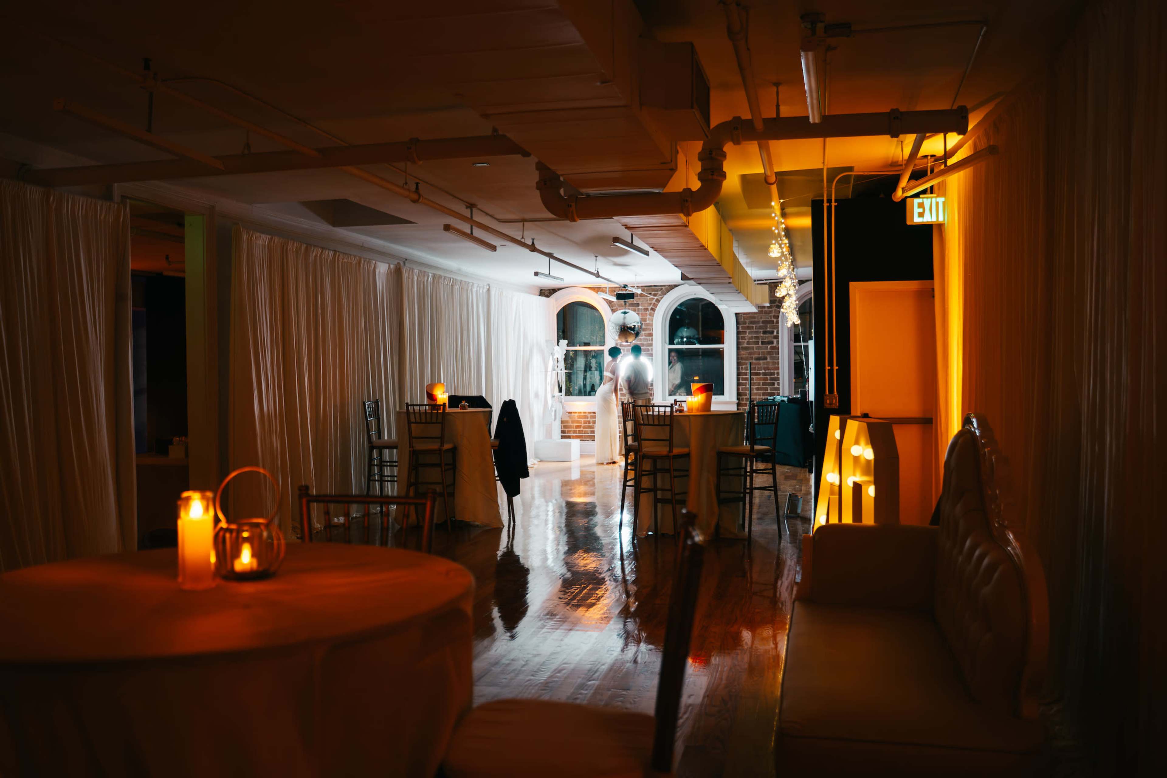 The scene shows an elegantly designed event hall with tables, candles, and soft lighting under draped fabric partitions.