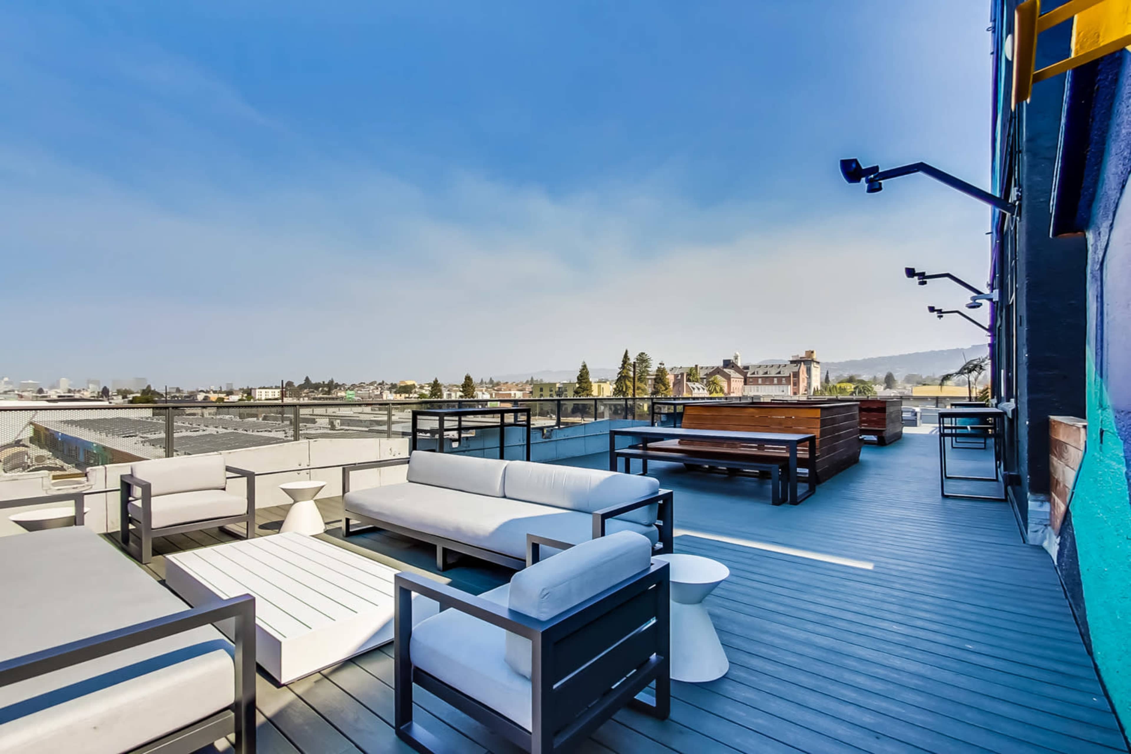 A spacious rooftop terrace featuring modern seating areas and wooden tables with a view of a city landscape.