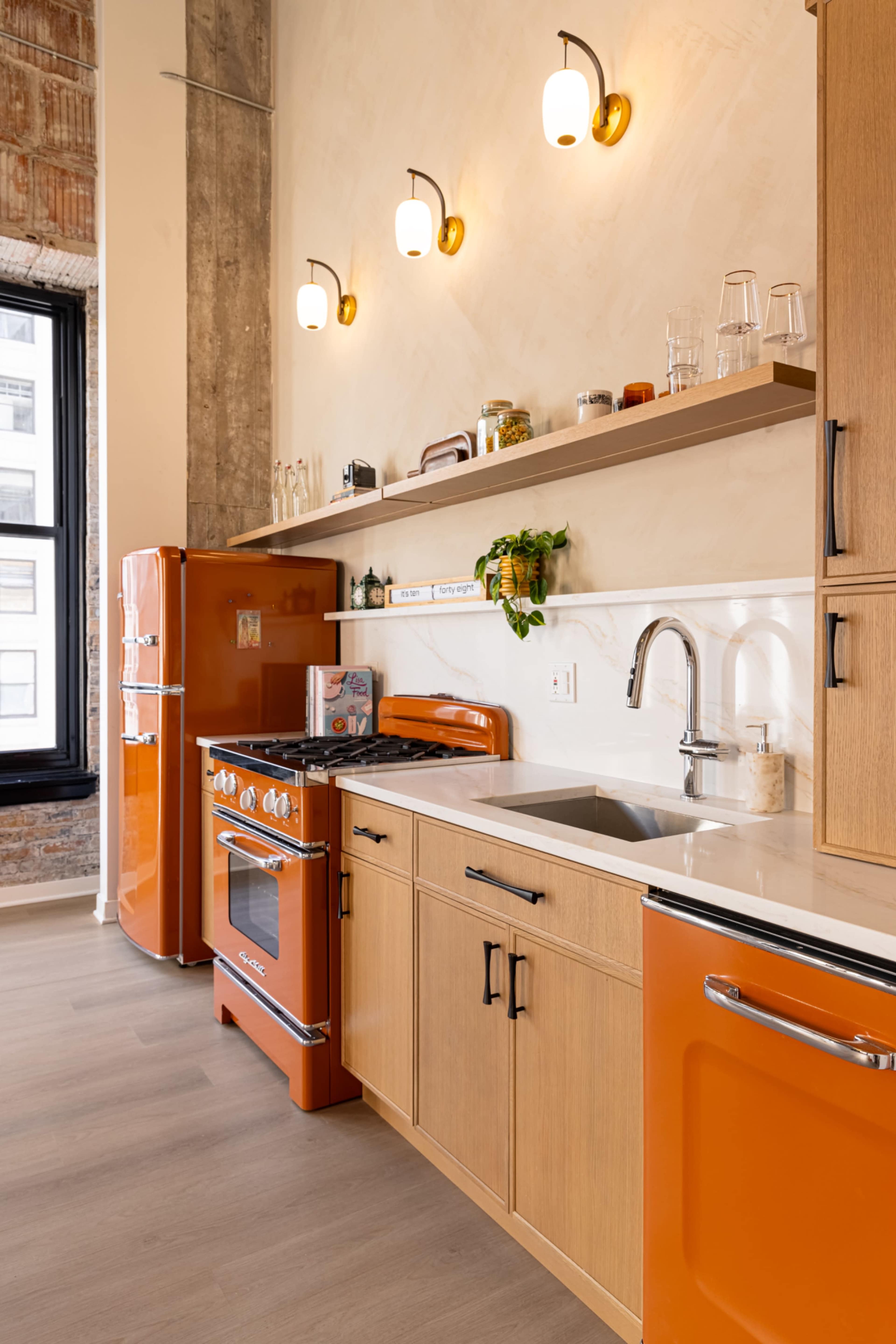 The kitchen features orange cabinetry, a vintage-style refrigerator, and a stove, all complemented by wooden shelves and modern lighting.
