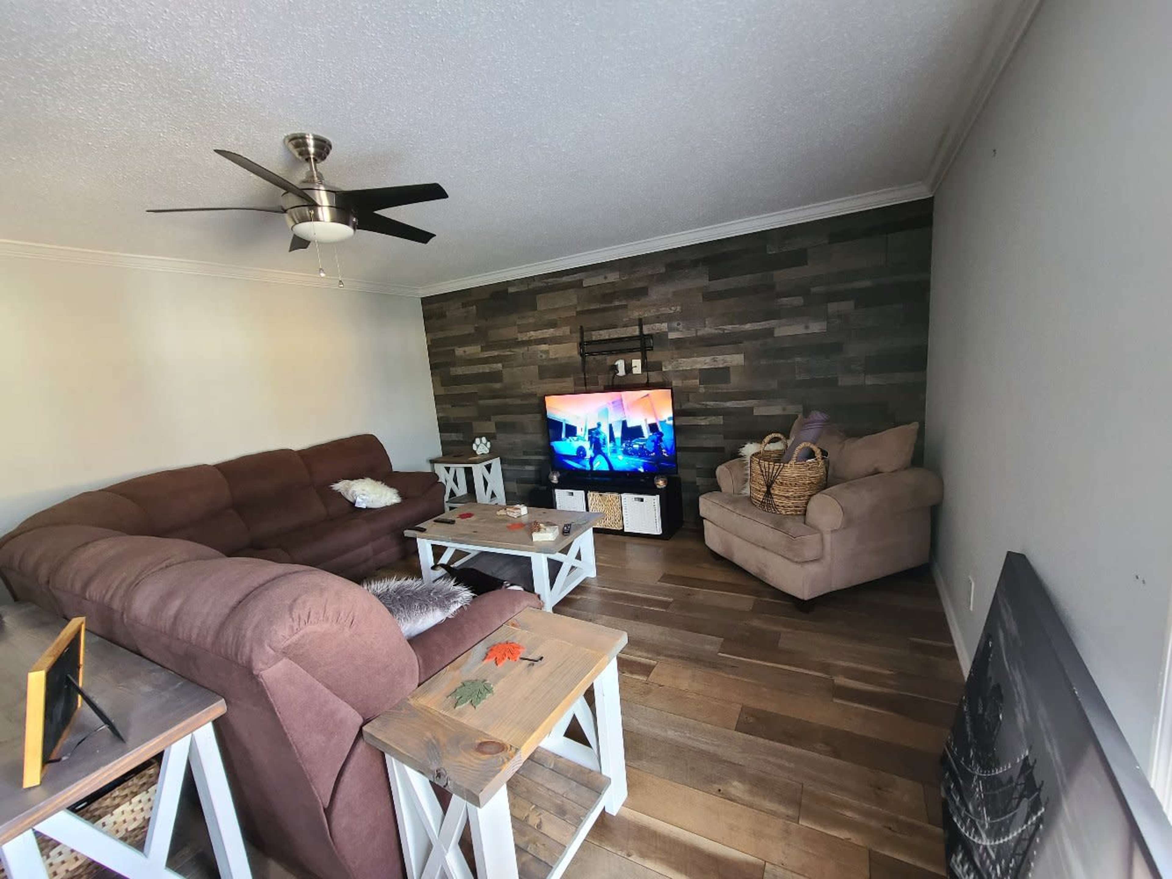 The living room features a brown sectional sofa, a beige armchair, a wooden coffee table, and a television mounted on a stone accent wall.