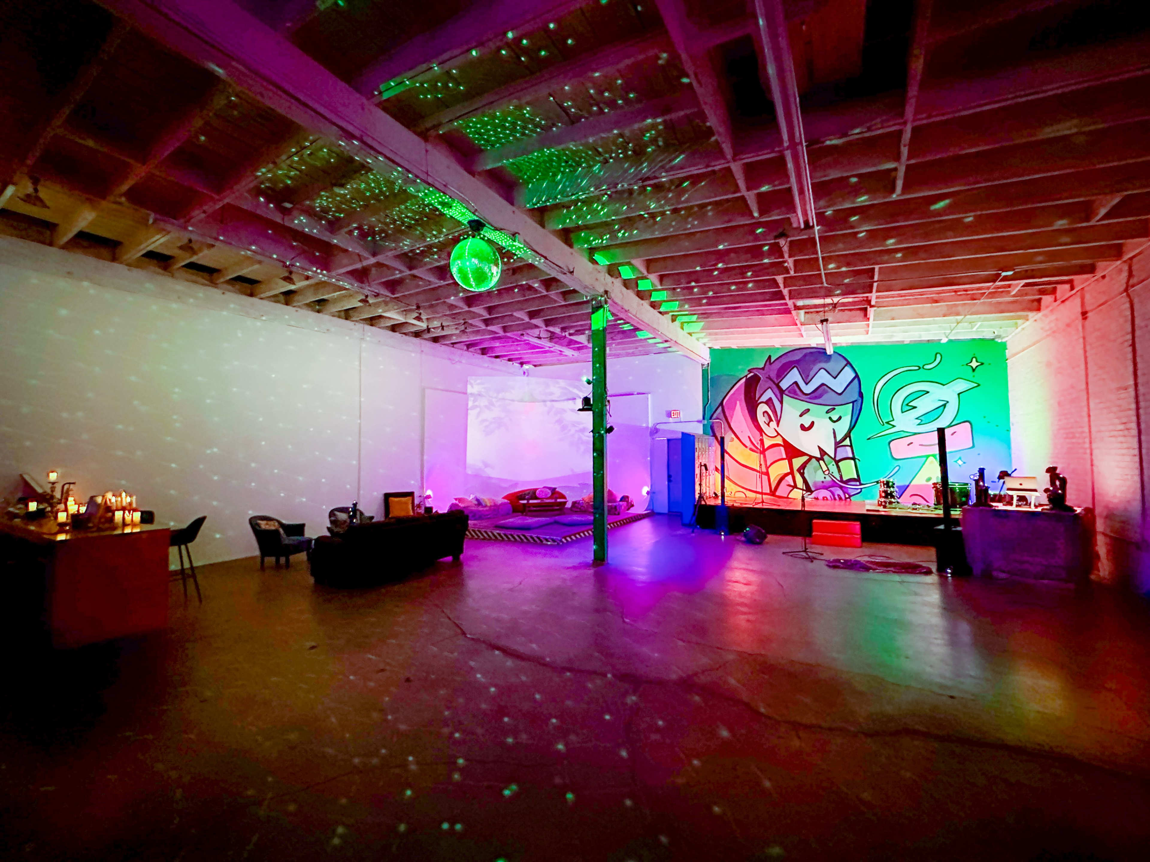 A spacious room features a large mural of a character, colorful lighting effects, and a seating area with various furnishings.