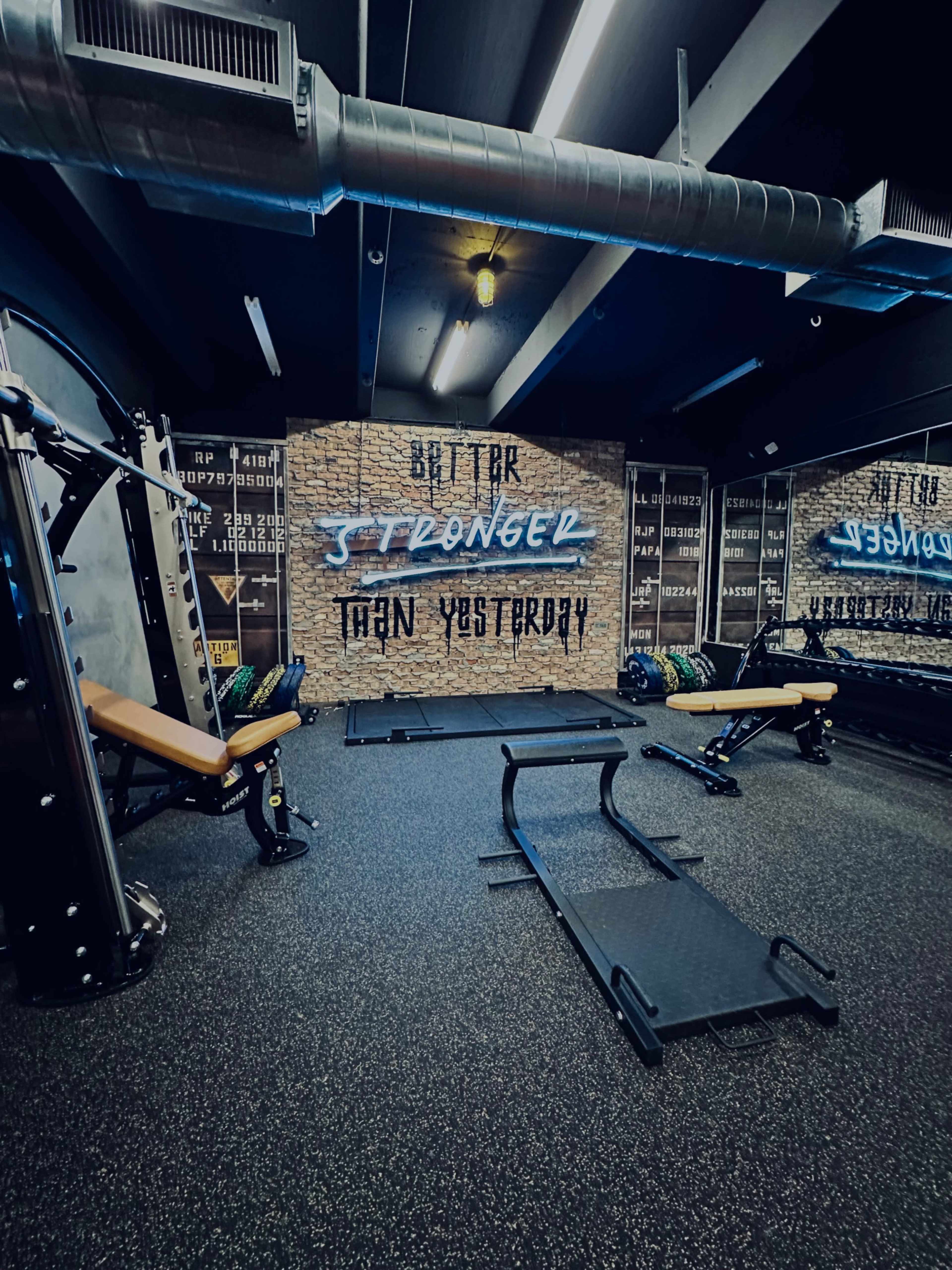 A gym interior featuring weightlifting equipment, a mirrored wall, and motivational phrases painted on the wall.
