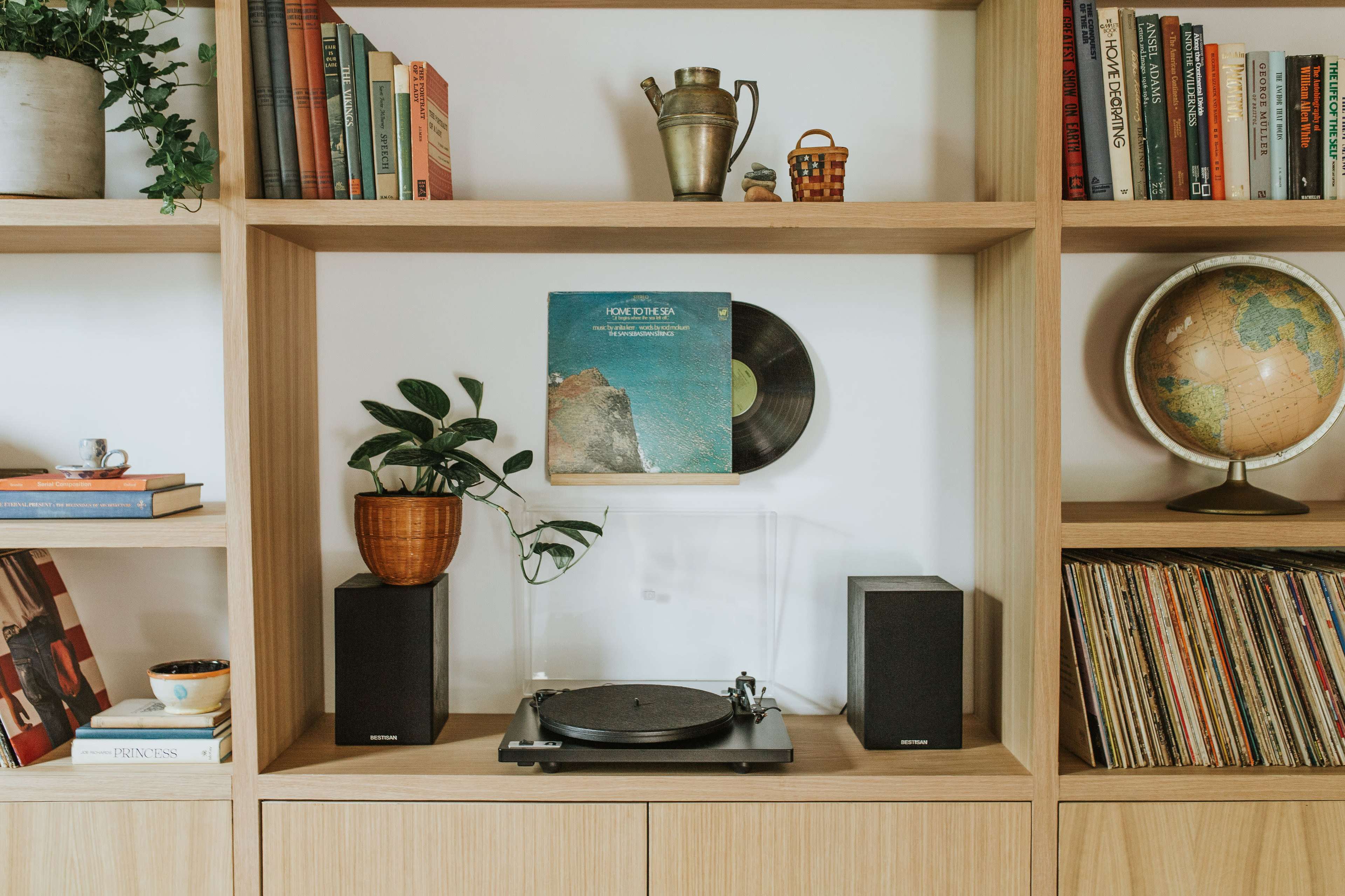 A wooden bookshelf displays books, a globe, a houseplant, and a turntable with a vinyl record on its stand.