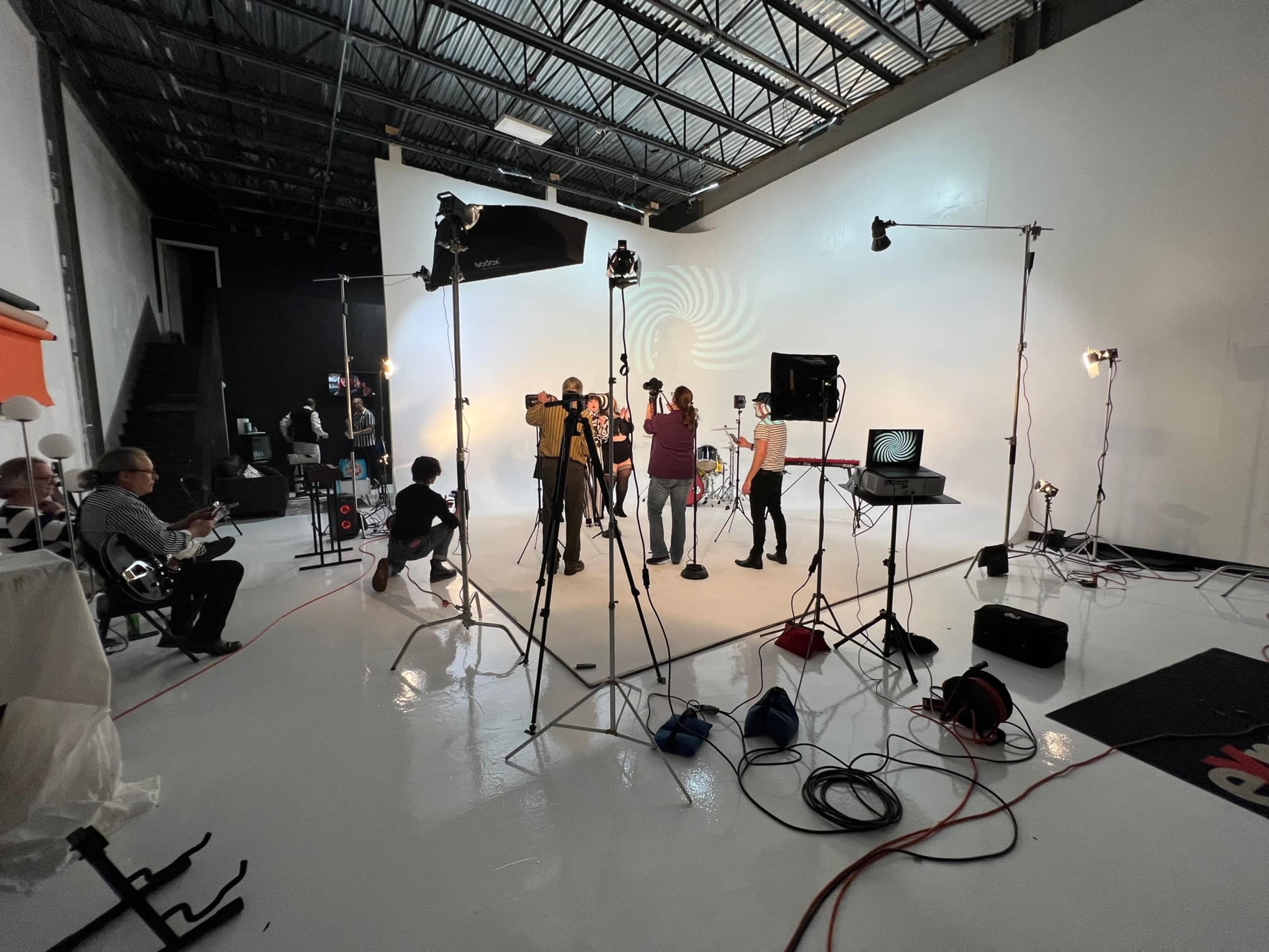 A photo studio is set up with a crew filming a music video, surrounded by various lighting and audio equipment.