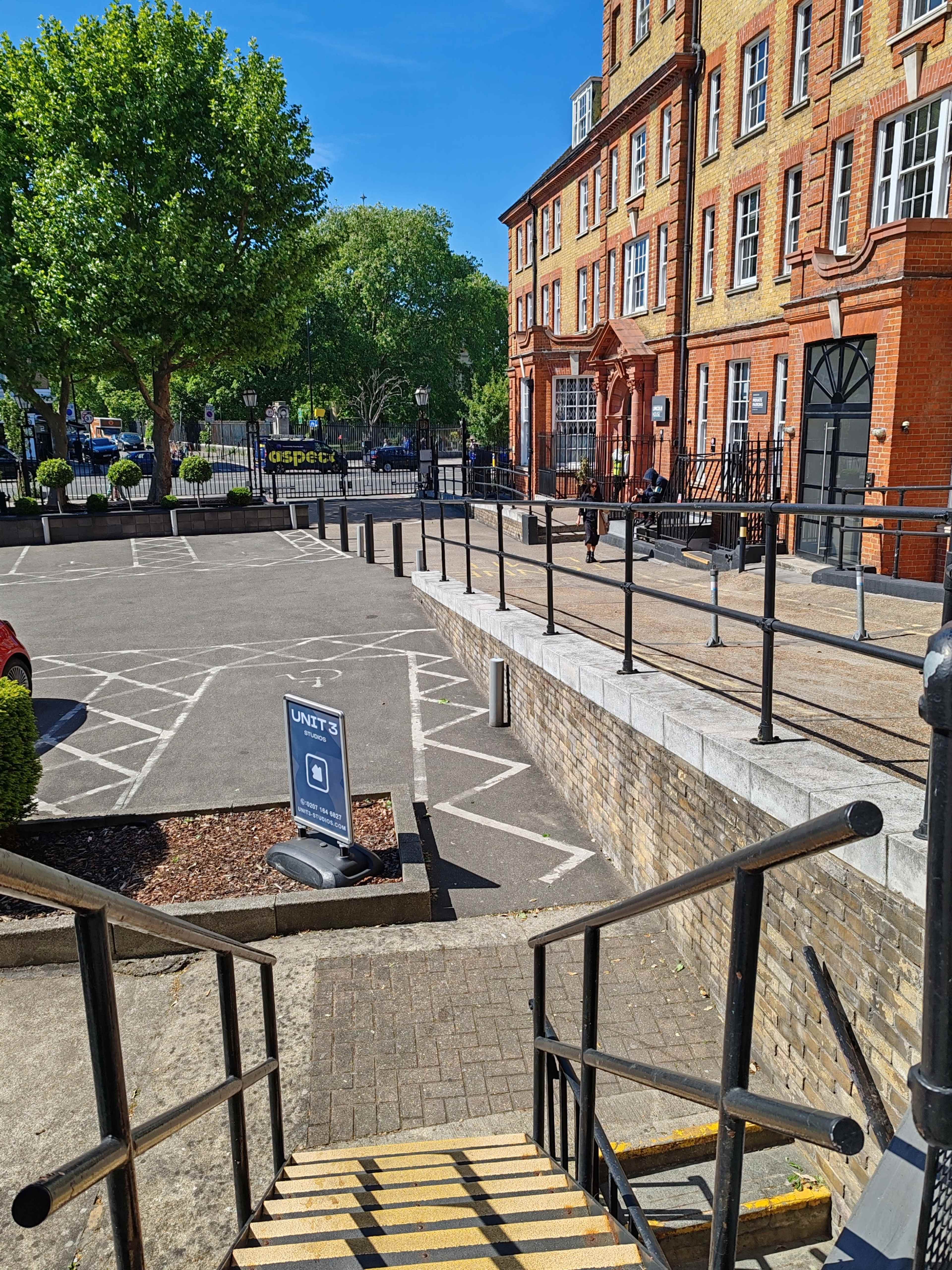 The image shows a set of stairs leading down to a parking area beside a brick building with large windows and a red facade.