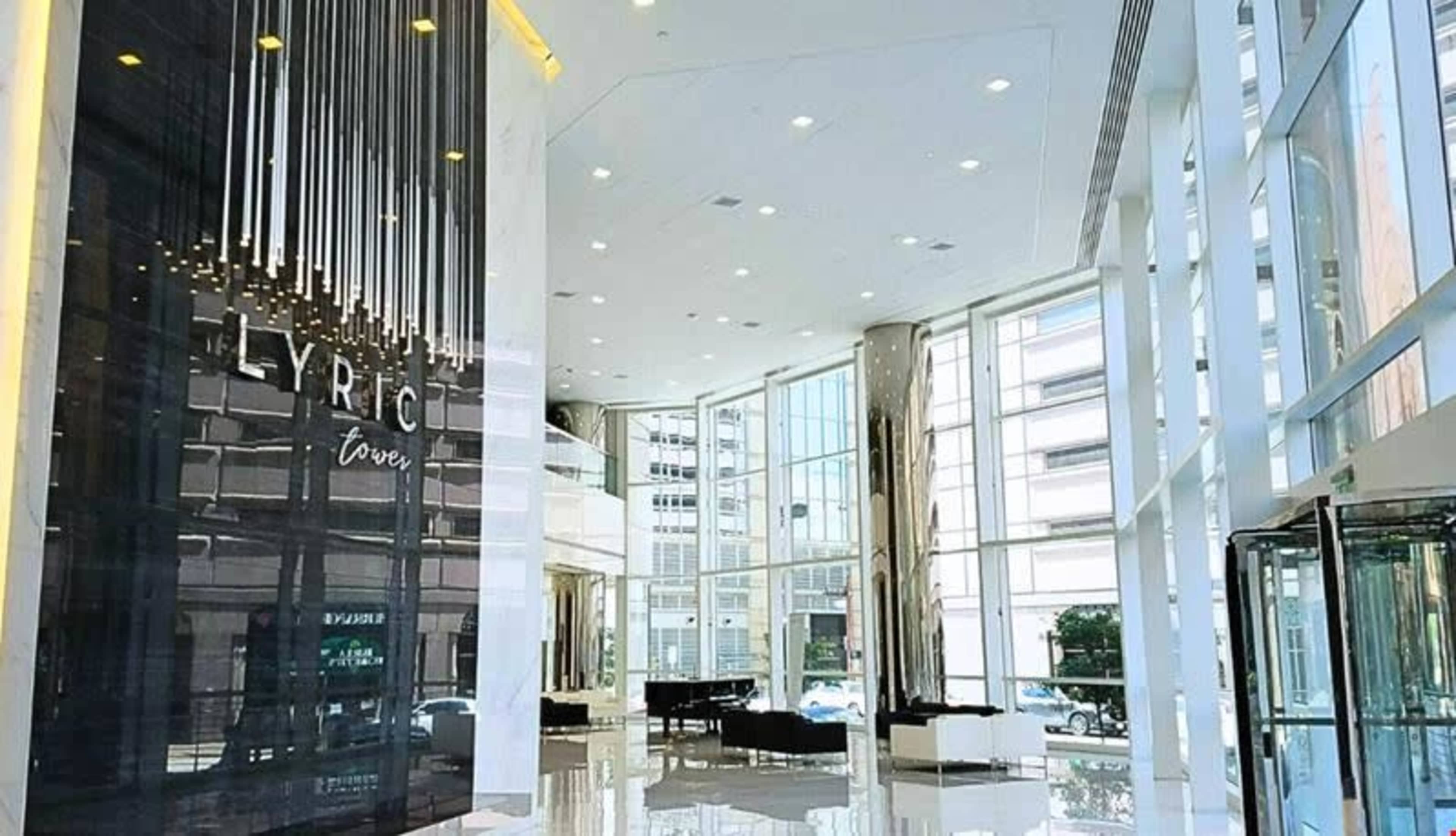 The image shows a modern hotel lobby with large windows, sleek marble flooring, and a wall featuring the name "LYRIC Tower."