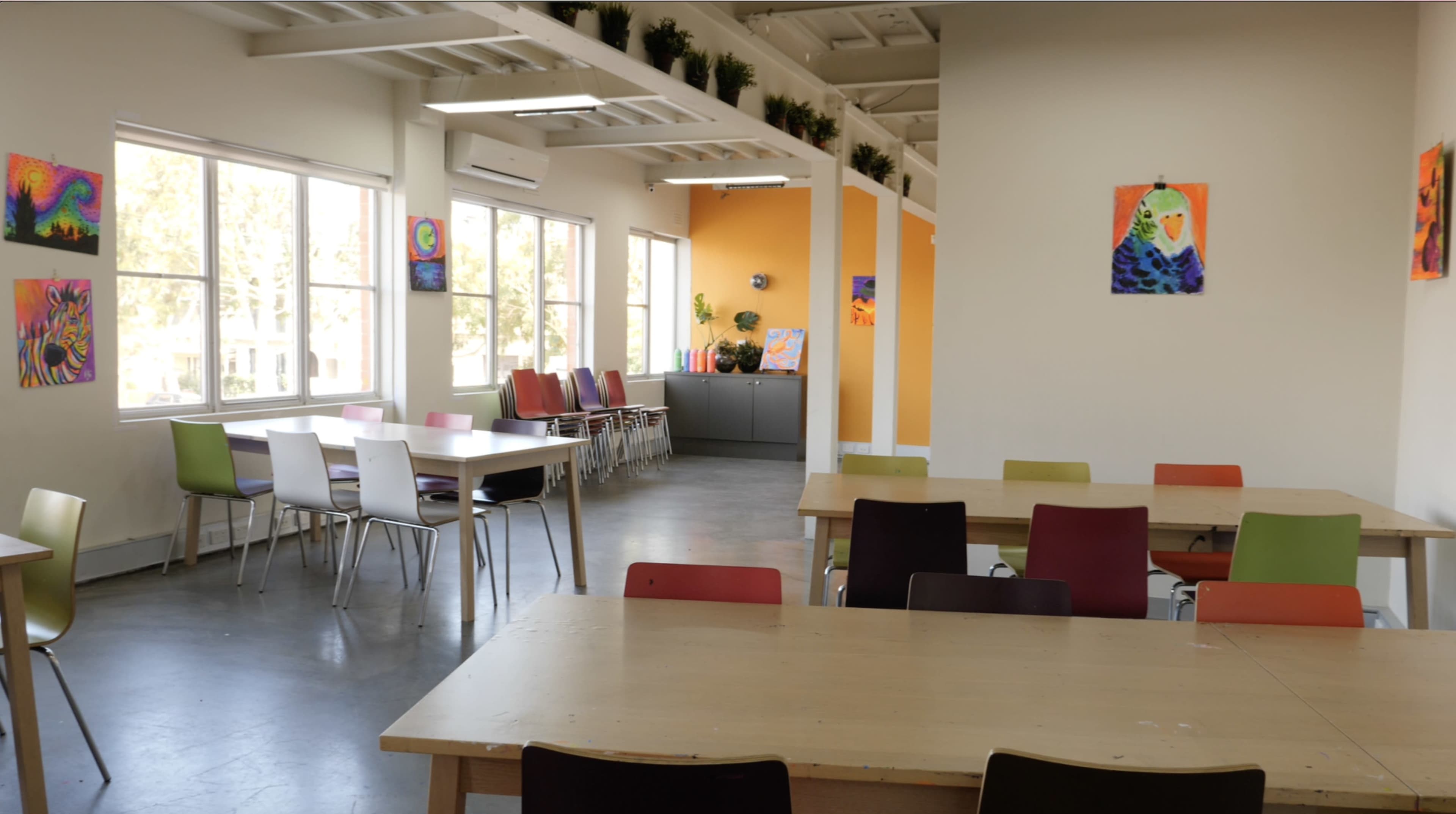 A modern classroom with tables and chairs arranged along with colorful artwork displayed on the walls.