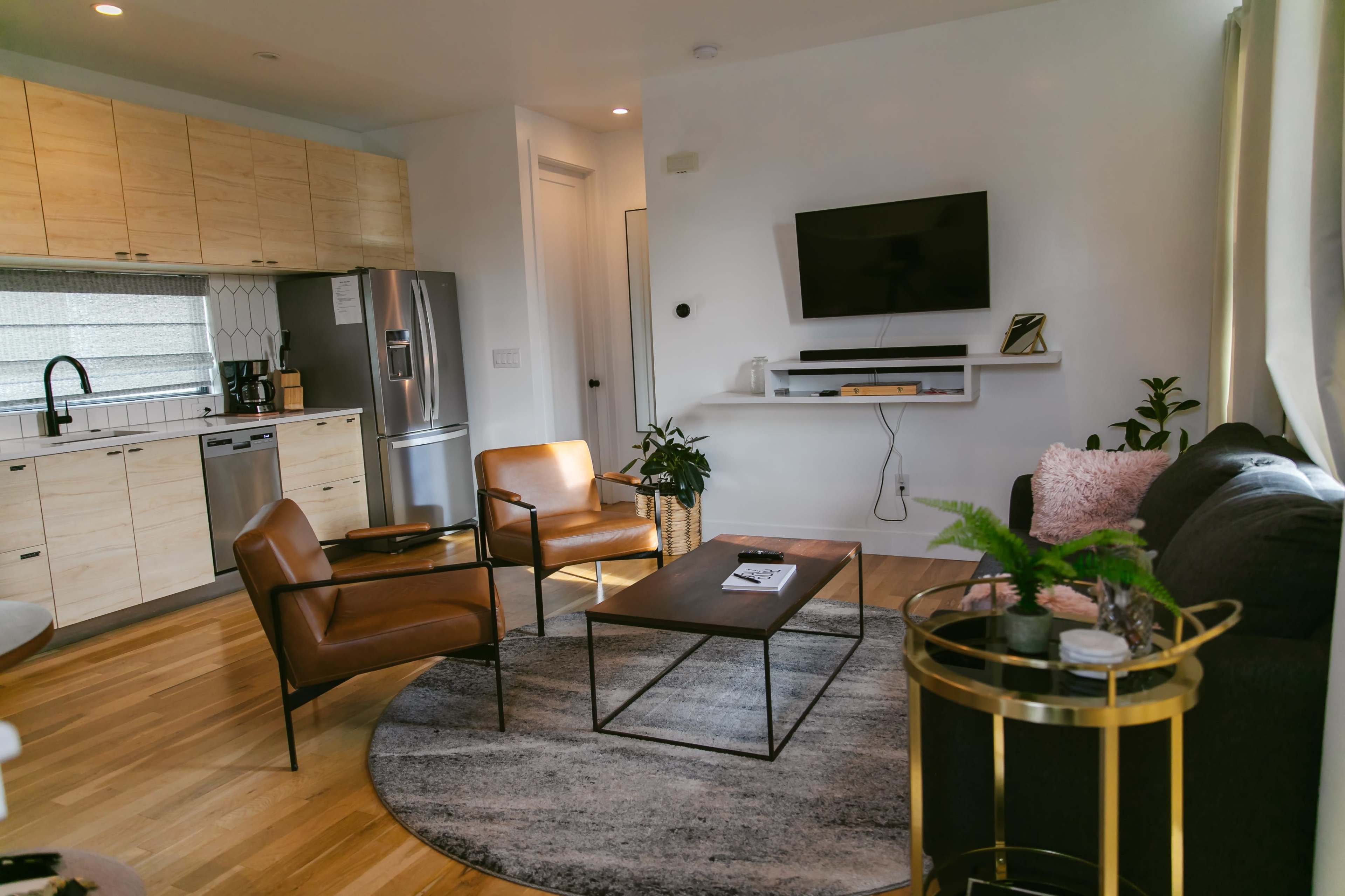 The living room features a modern layout with a circular rug, two leather chairs, a coffee table, a sofa, and a wall-mounted television.