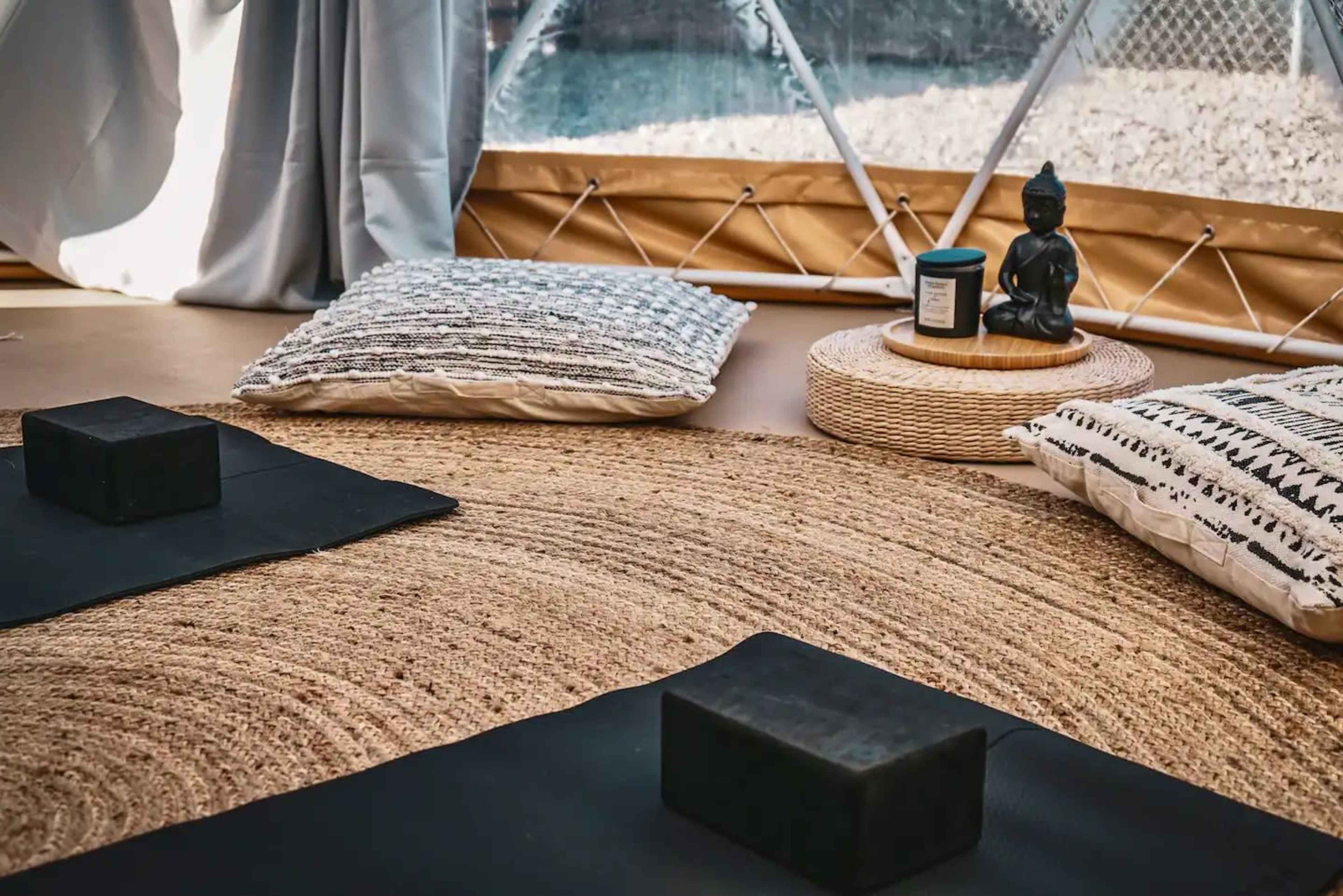 The scene features a cozy, tented space with yoga mats, decorative pillows, and a small statue of Buddha on a woven tray.