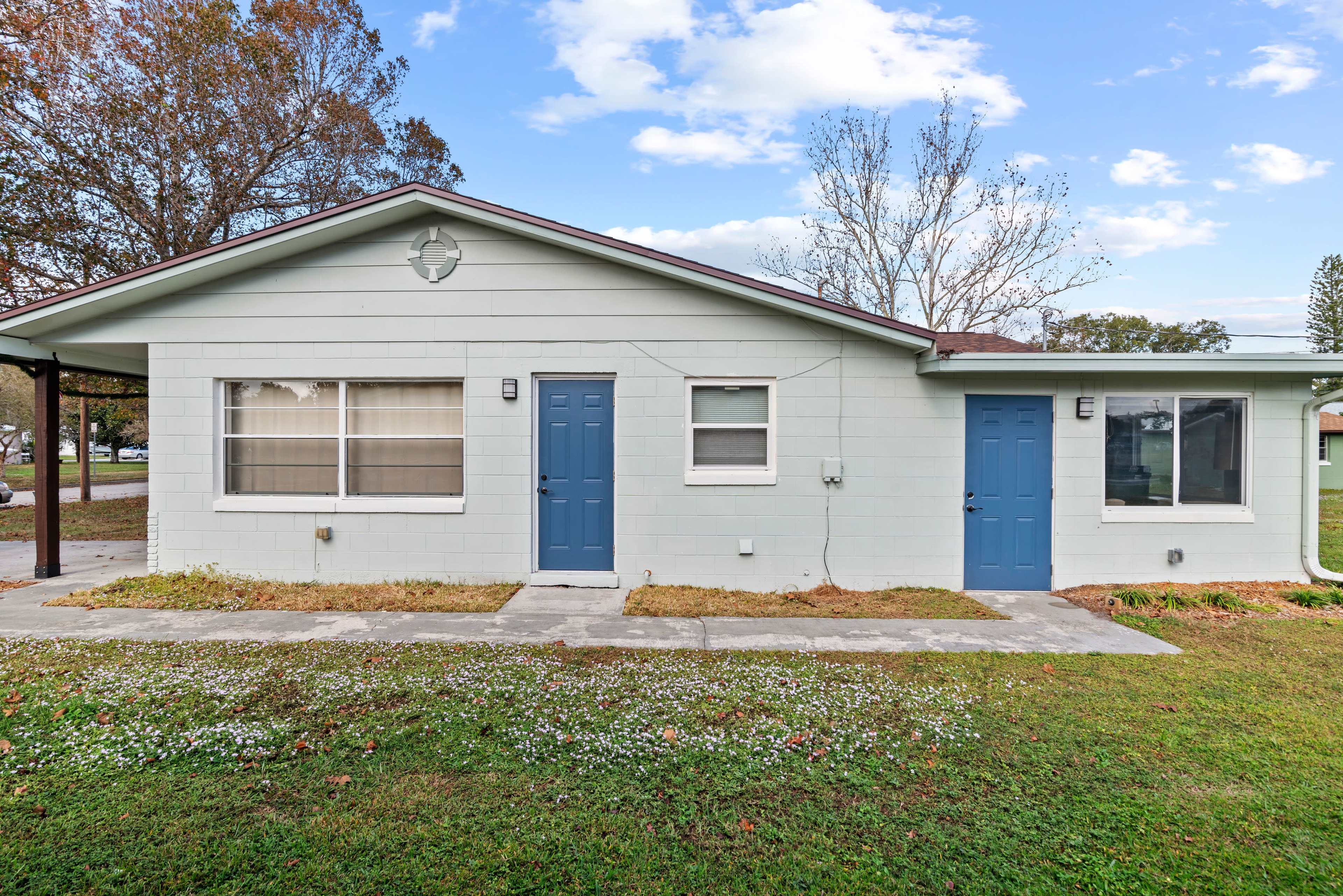 The image shows a light blue twin-unit residential building with two blue doors and a grassy front yard.