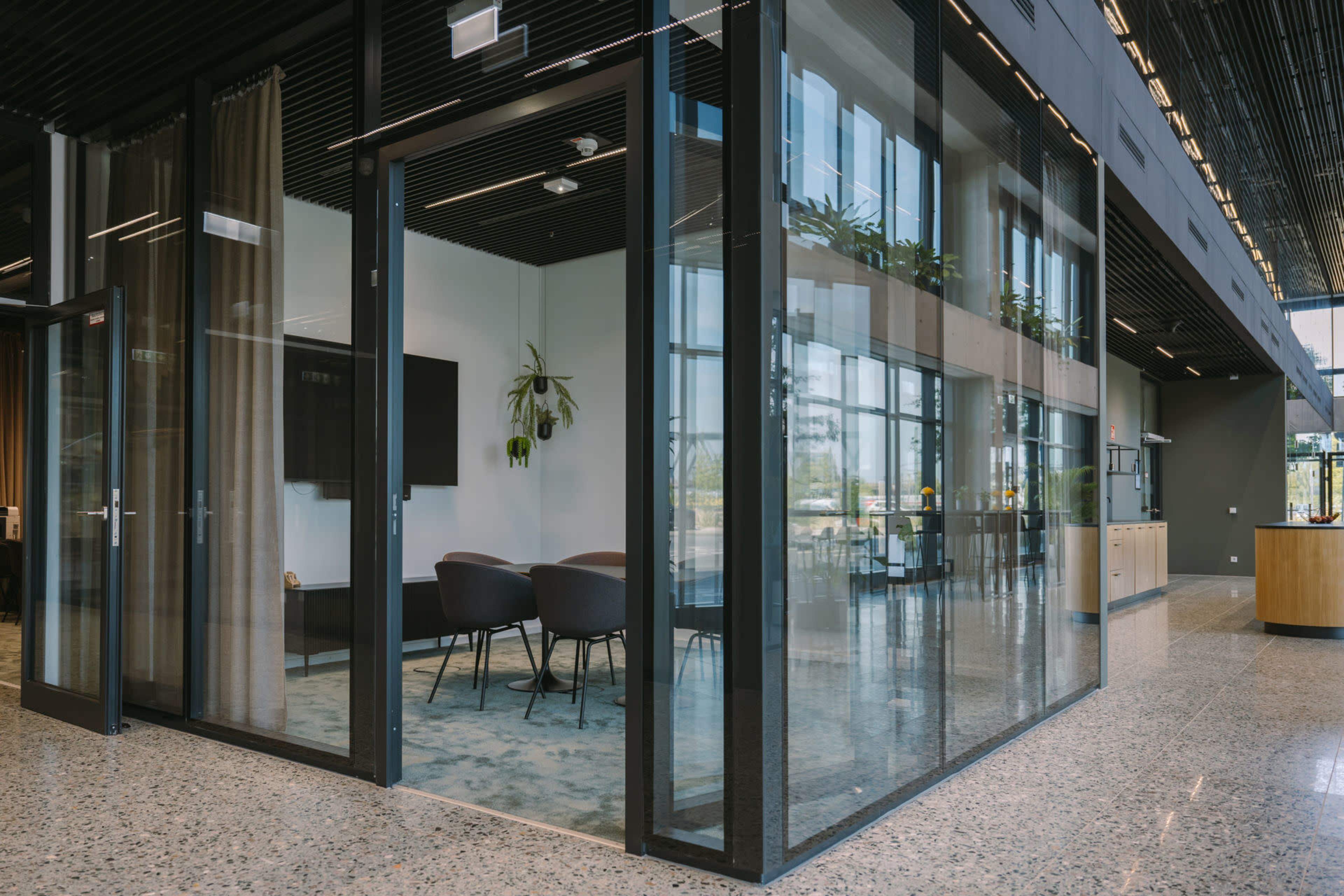 The image shows a modern office space featuring glass walls, a seating area with chairs, and a carpet on a polished floor.