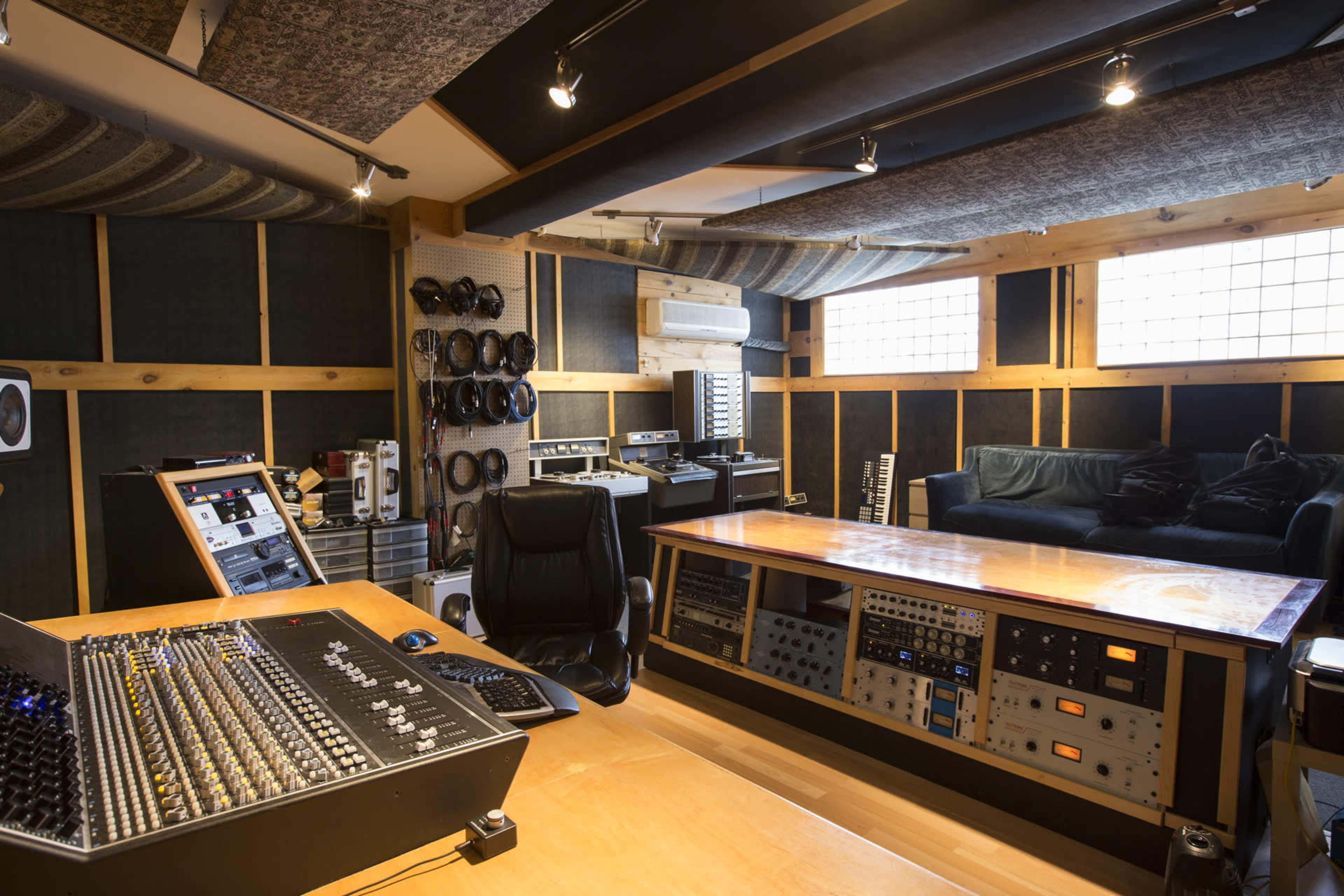 A music recording studio features a large mixing console, various audio equipment, and a comfortable seating area.