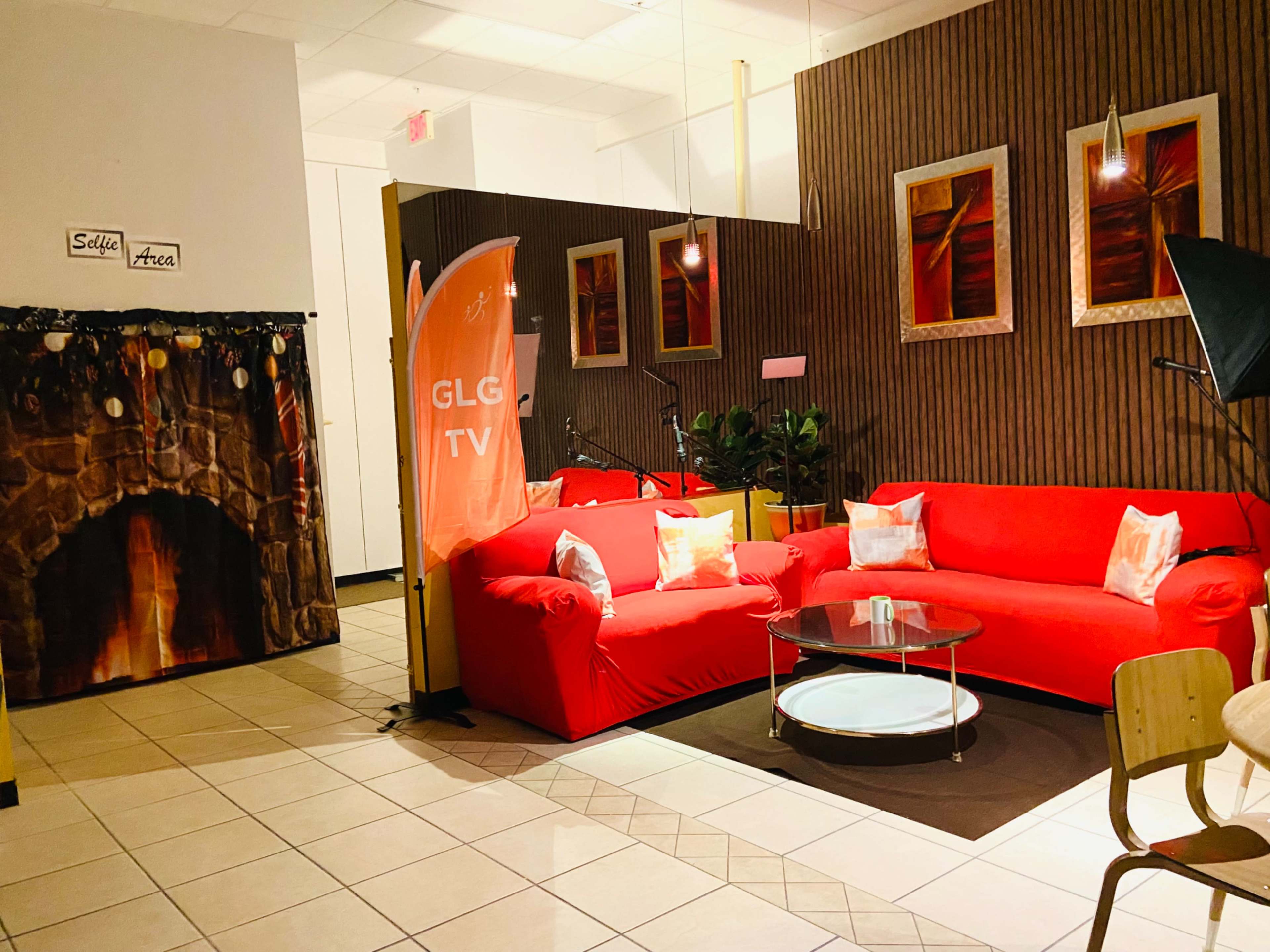 A seating area with red couches, a glass coffee table, a decorative fireplace backdrop, and framed art on the walls.