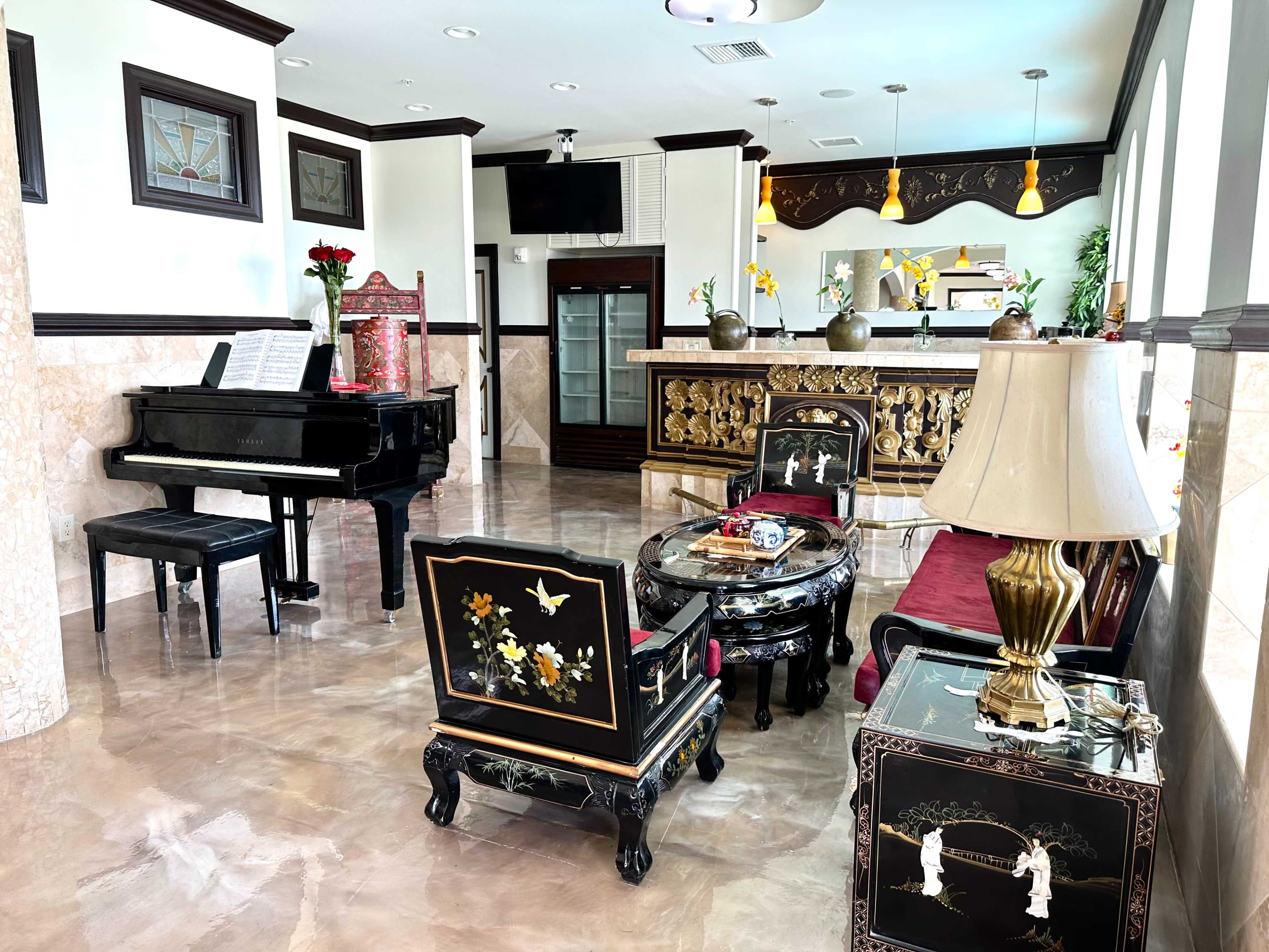 A spacious, elegantly furnished lounge area featuring a piano, a bar, and ornate seating arrangements.