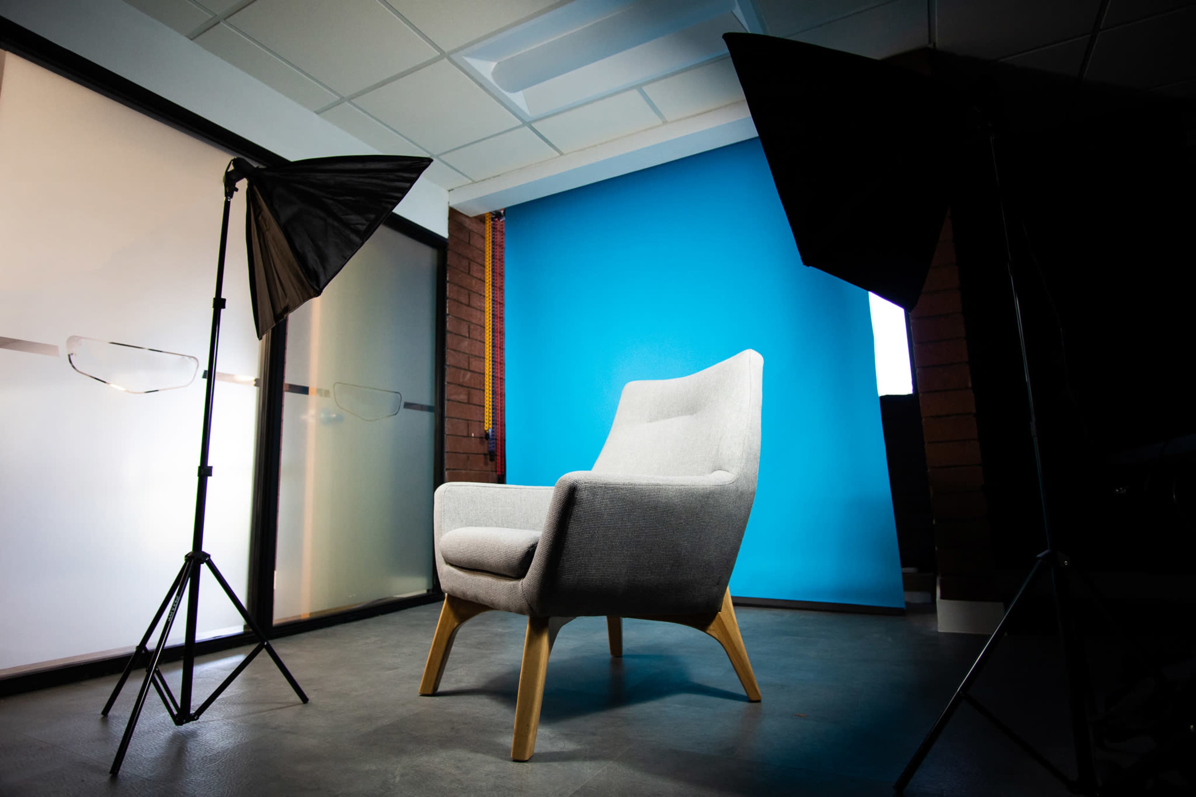A gray armchair positioned in front of a bright blue backdrop, with two softbox studio lights on either side.