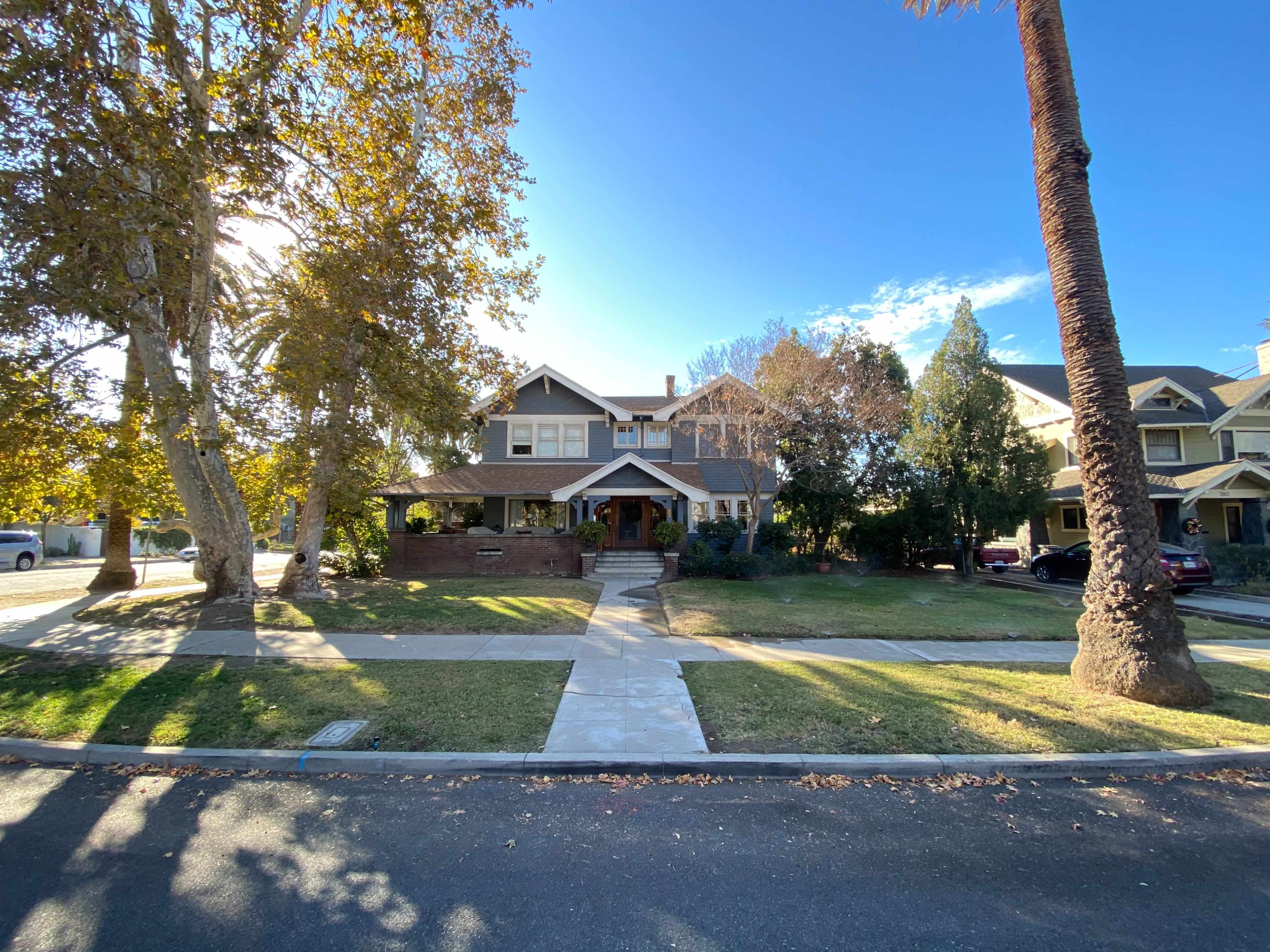 A large two-story house with a front porch is surrounded by a well-kept lawn and trees on a sunny day.