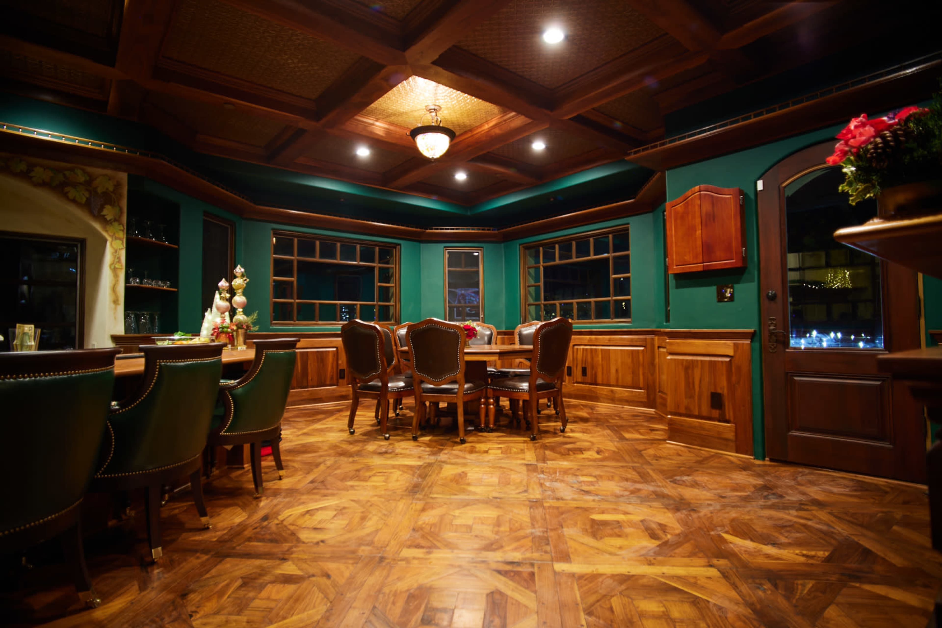 A wooden-paneled dining room with a round table and several chairs positioned near large windows.