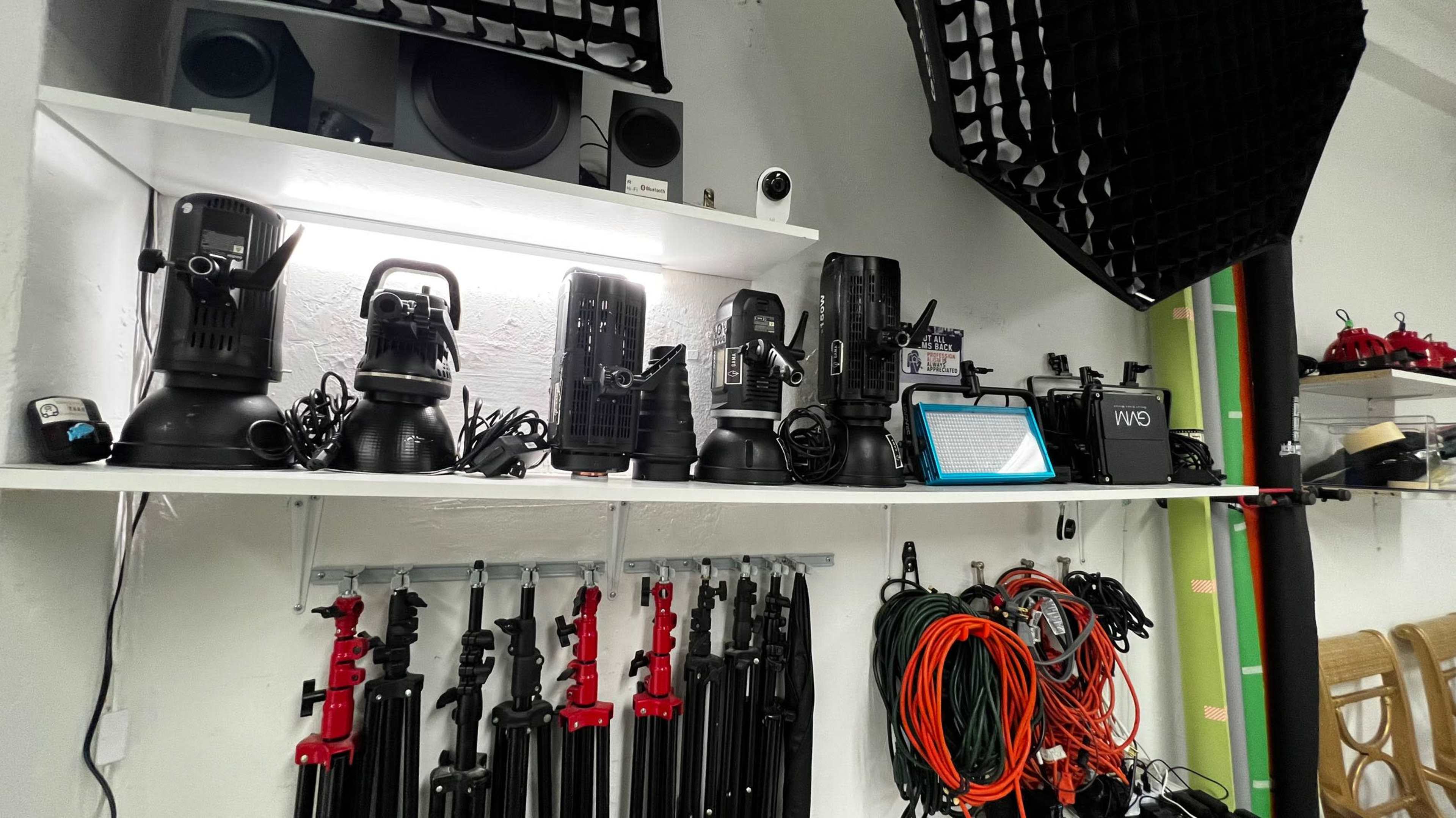 A collection of lighting equipment, tripods, and cables organized on shelves in a studio setup.